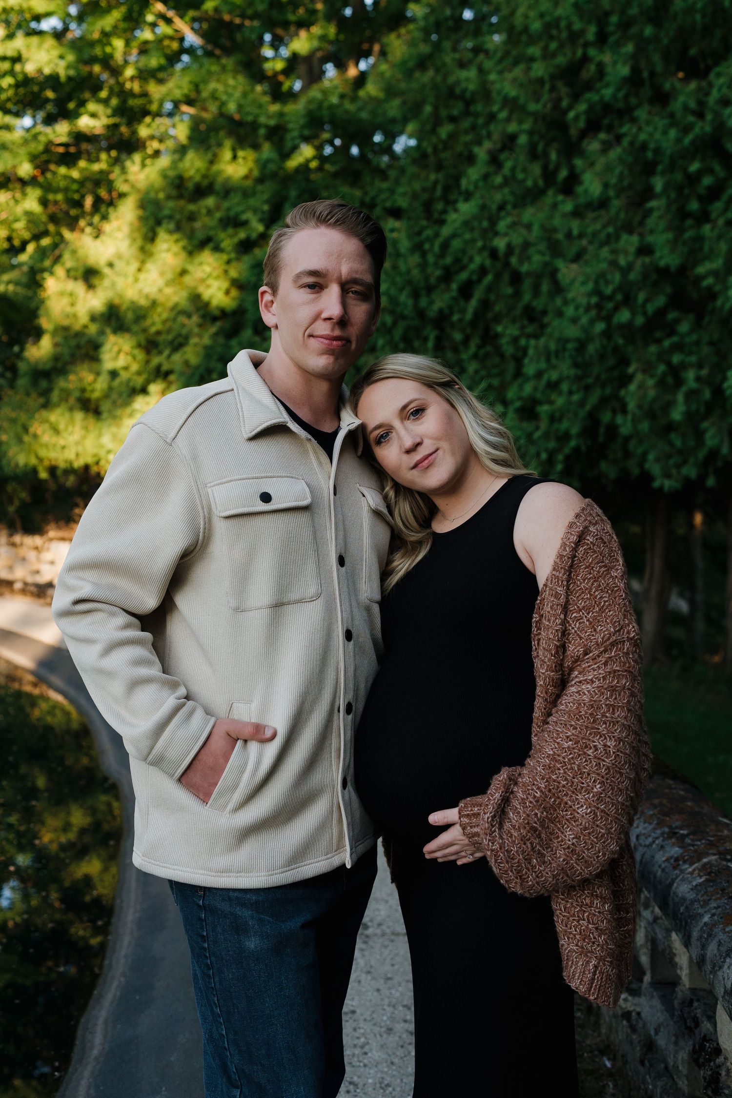 Couple embracing outdoors with lush green foliage in background during golden hour.