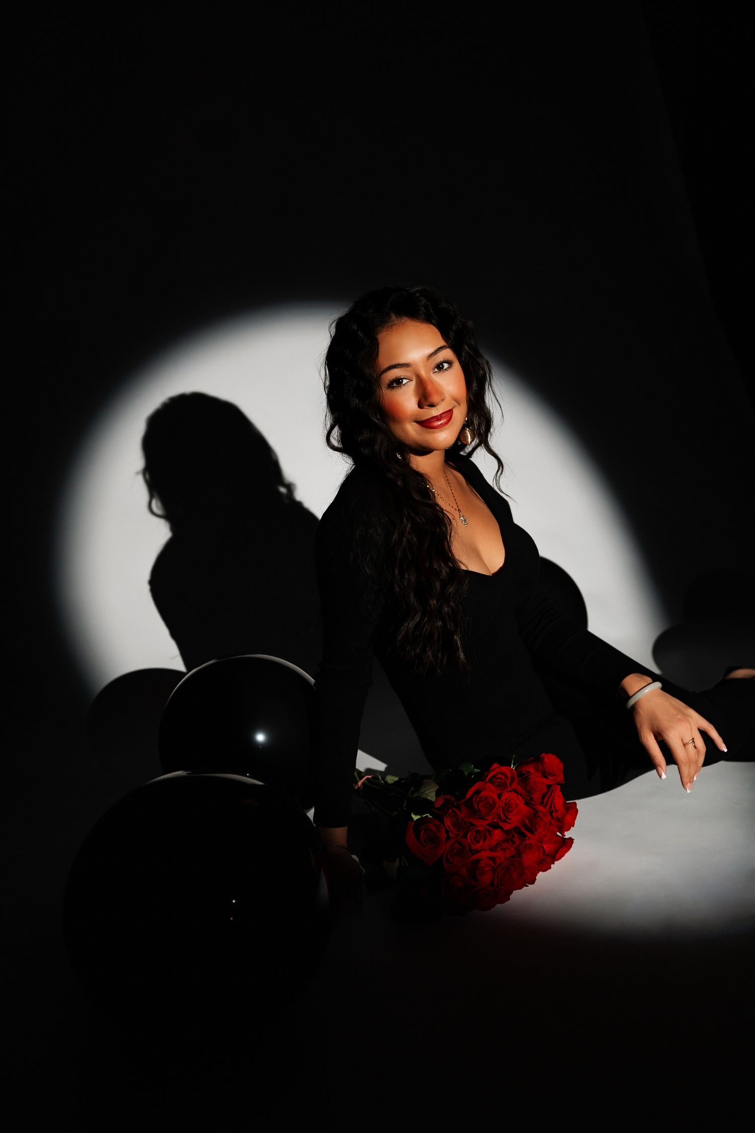 Elegant studio portrait with red roses and dramatic spotlight effect.