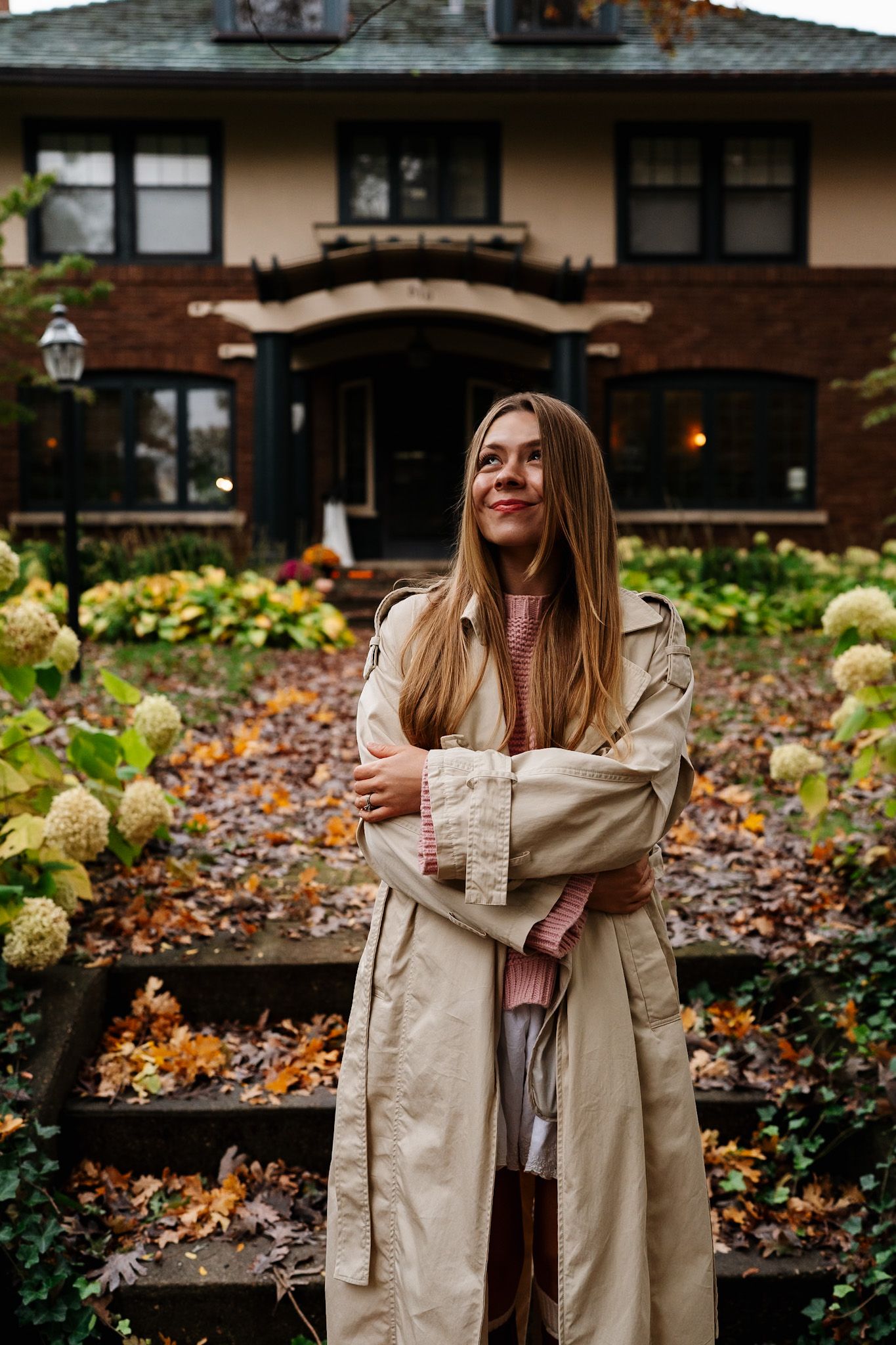 Candid autumn fashion moments captured in front of a traditional brick house with landscaped gardens.
