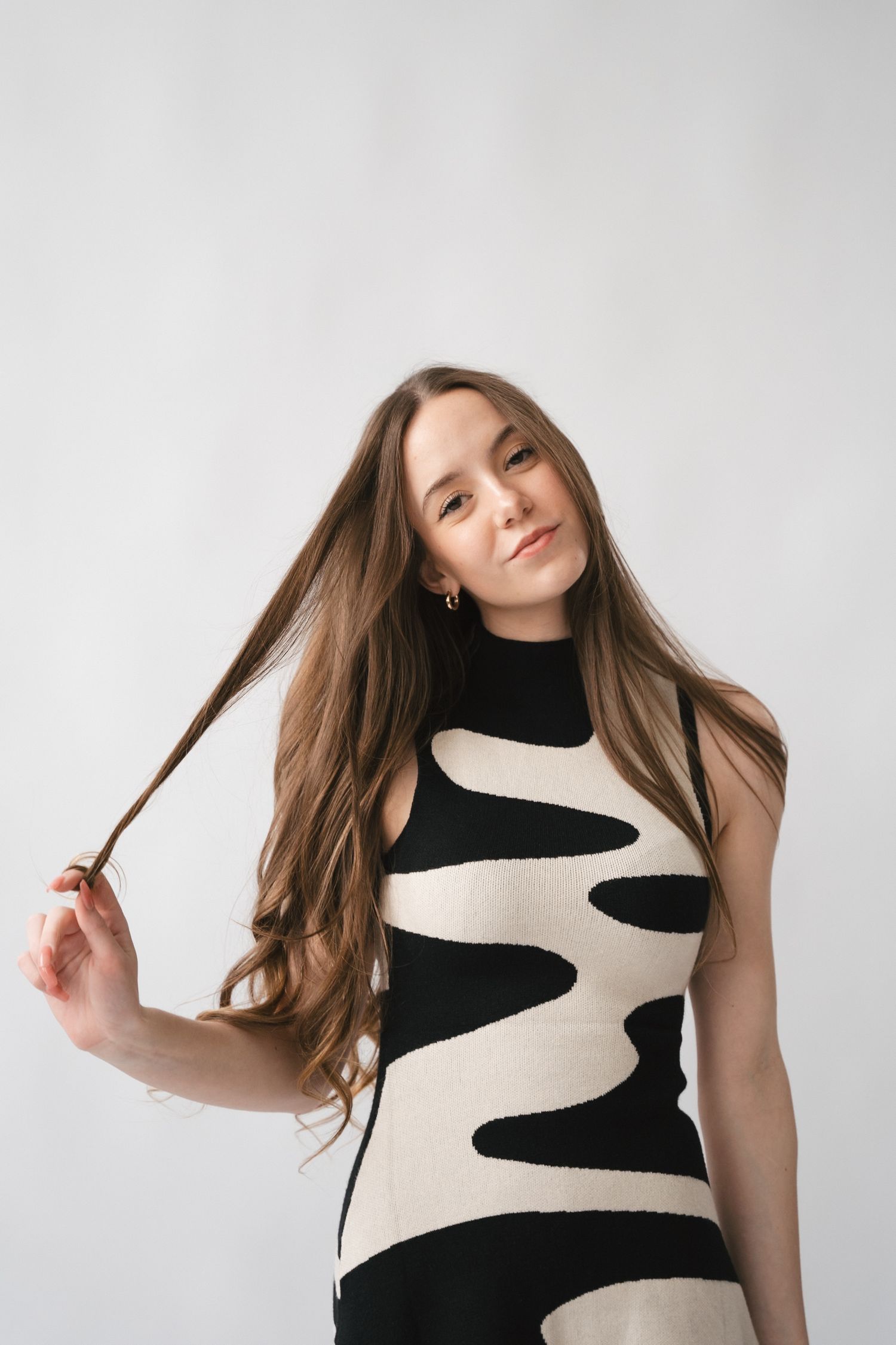 Woman in black and white geometric pattern dress tosses hair against white backdrop.