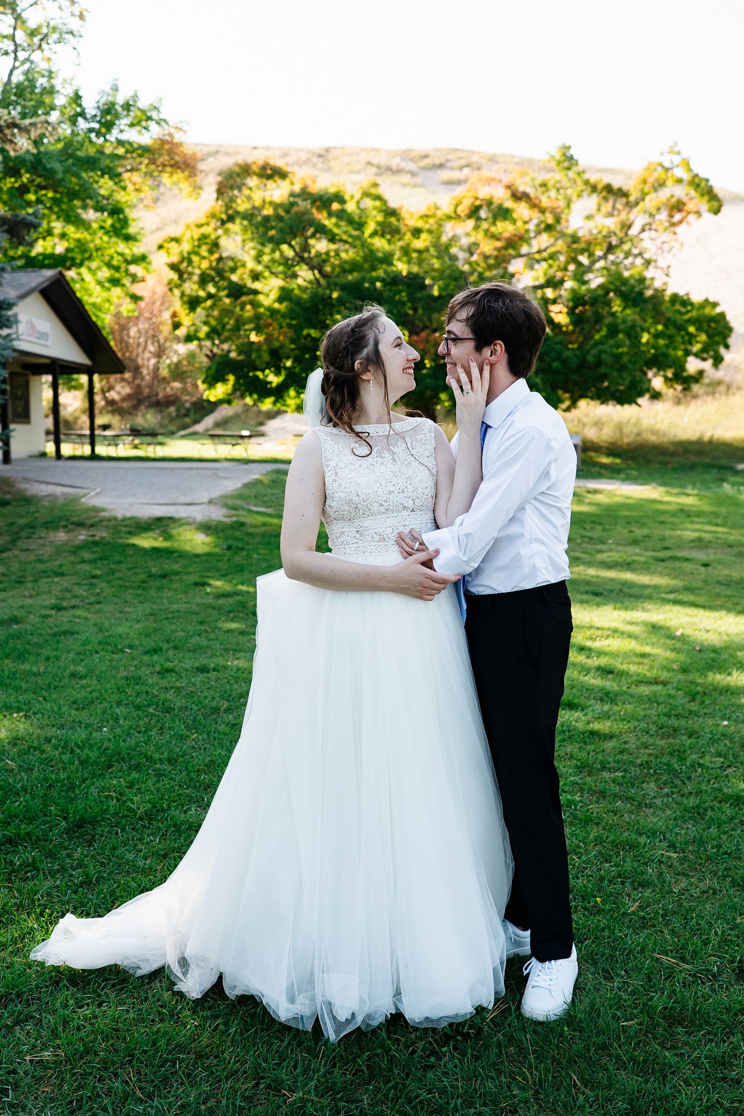 Wedding couple embraces on sunny lawn during outdoor photo session.