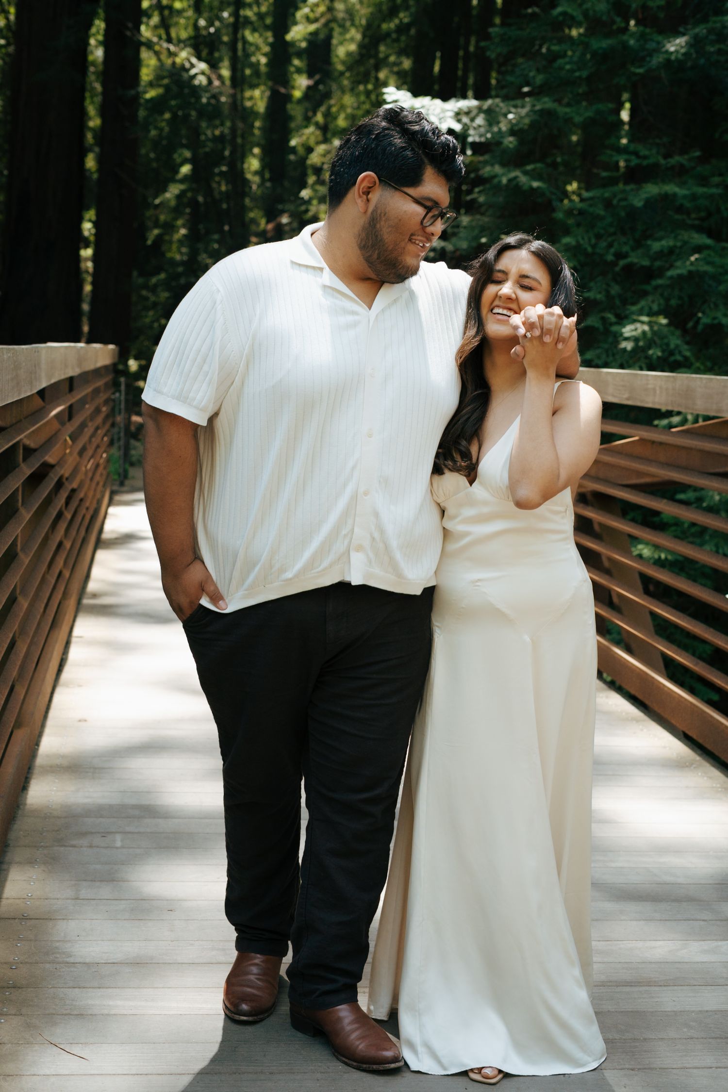 A joyful couple sharing a laugh together on a wooden bridge in a forest setting.