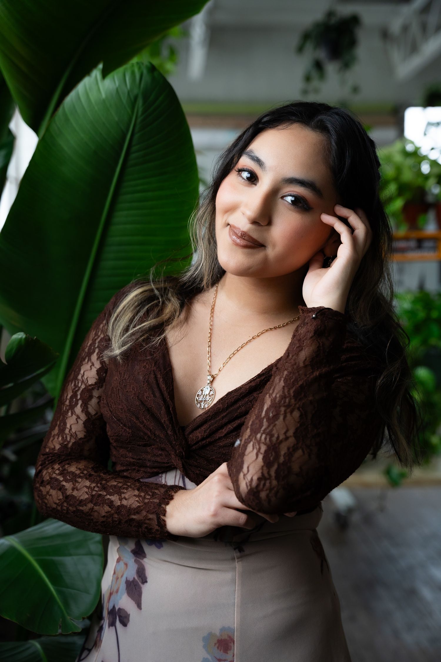 Artistic portrait with tropical leaves featuring brown lace top and delicate necklace.