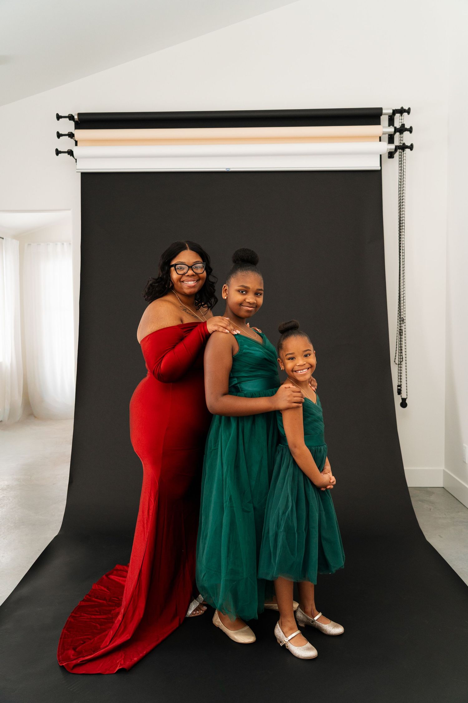 Three people pose together against a black backdrop wearing coordinating red and green formal dresses.