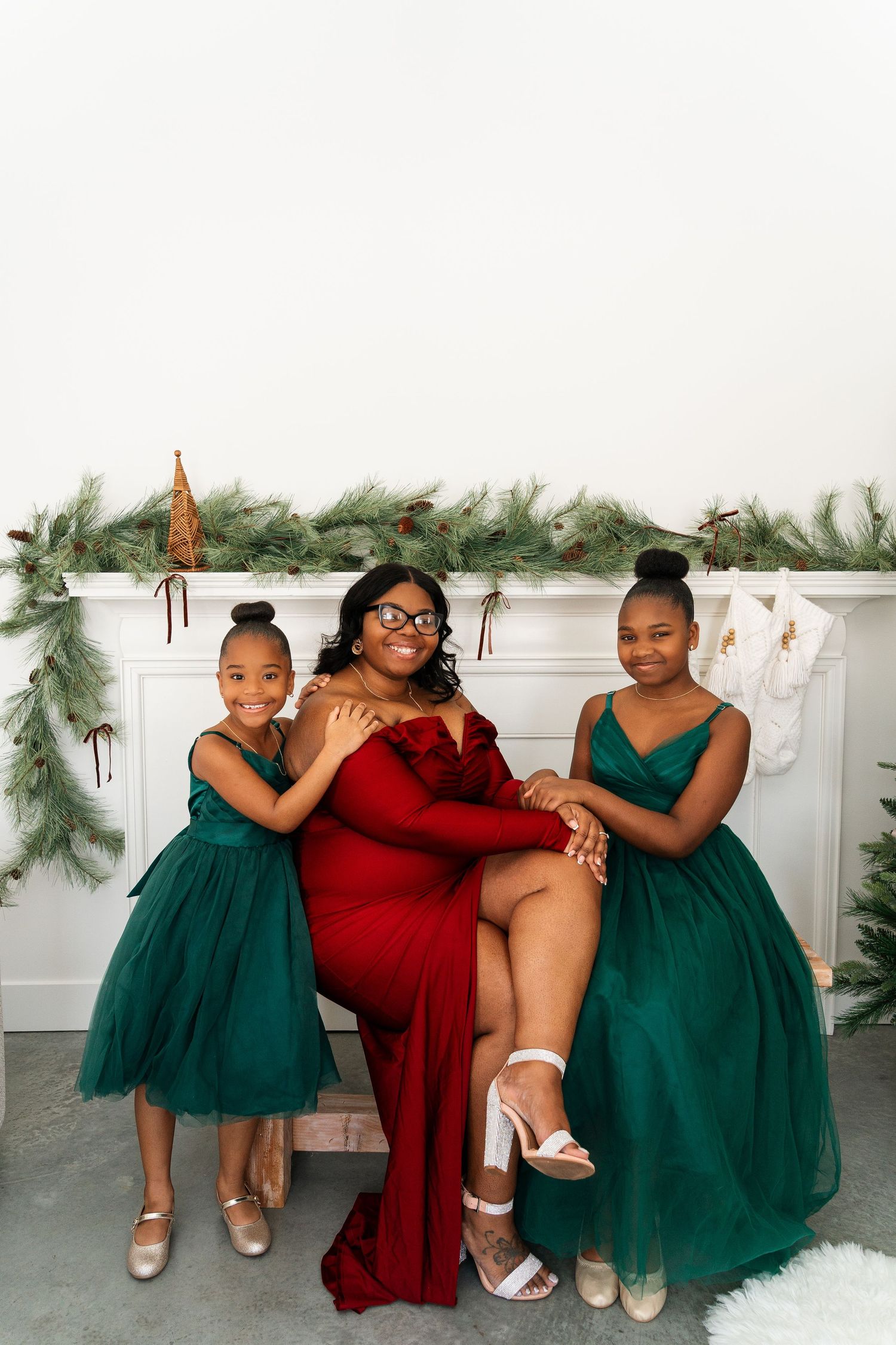 Holiday family portrait with emerald green and red dresses in front of decorated mantel.