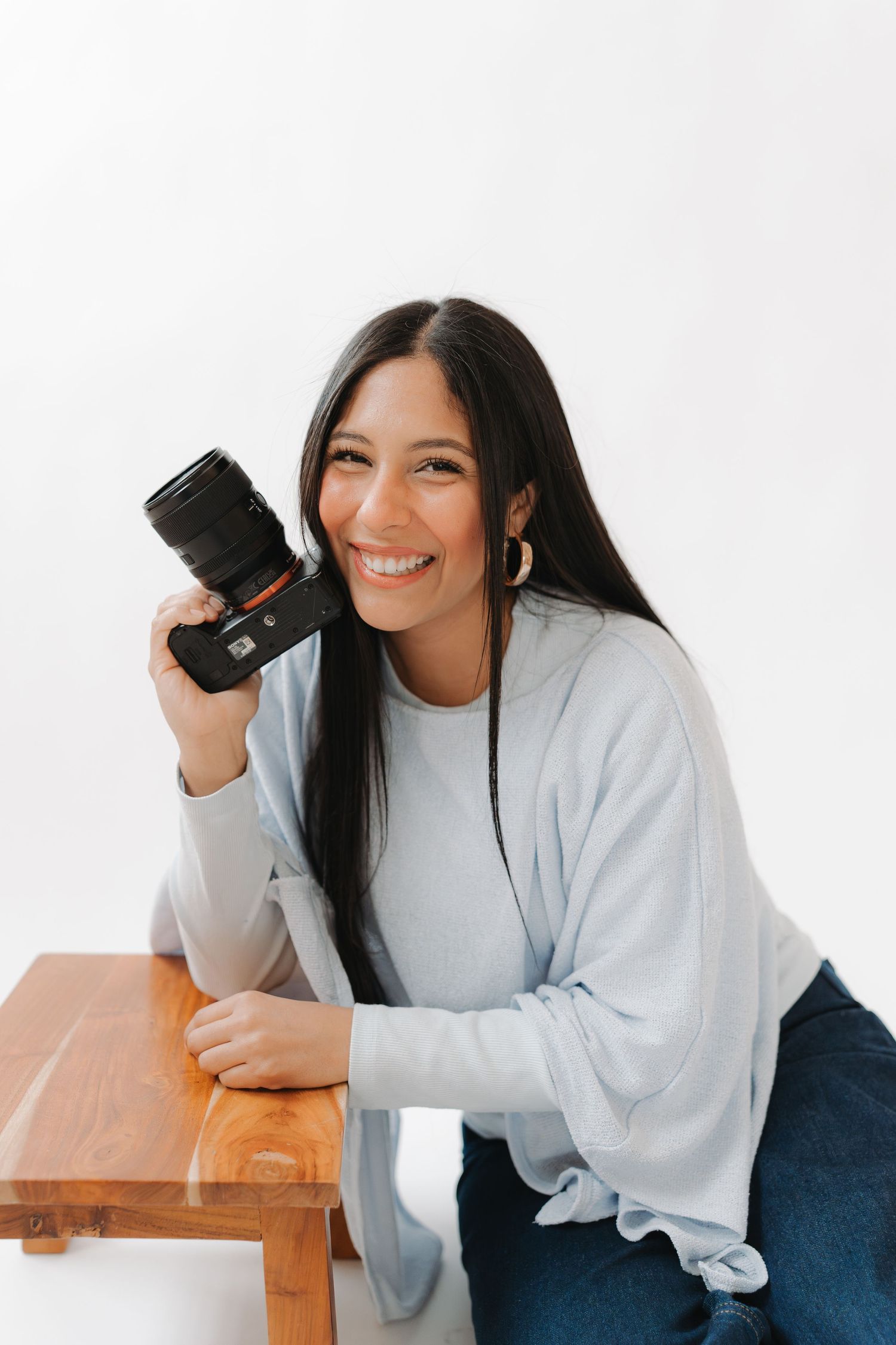 Person in light gray sweater and dark pants smiles while posing playfully in three different positions on wooden surface.