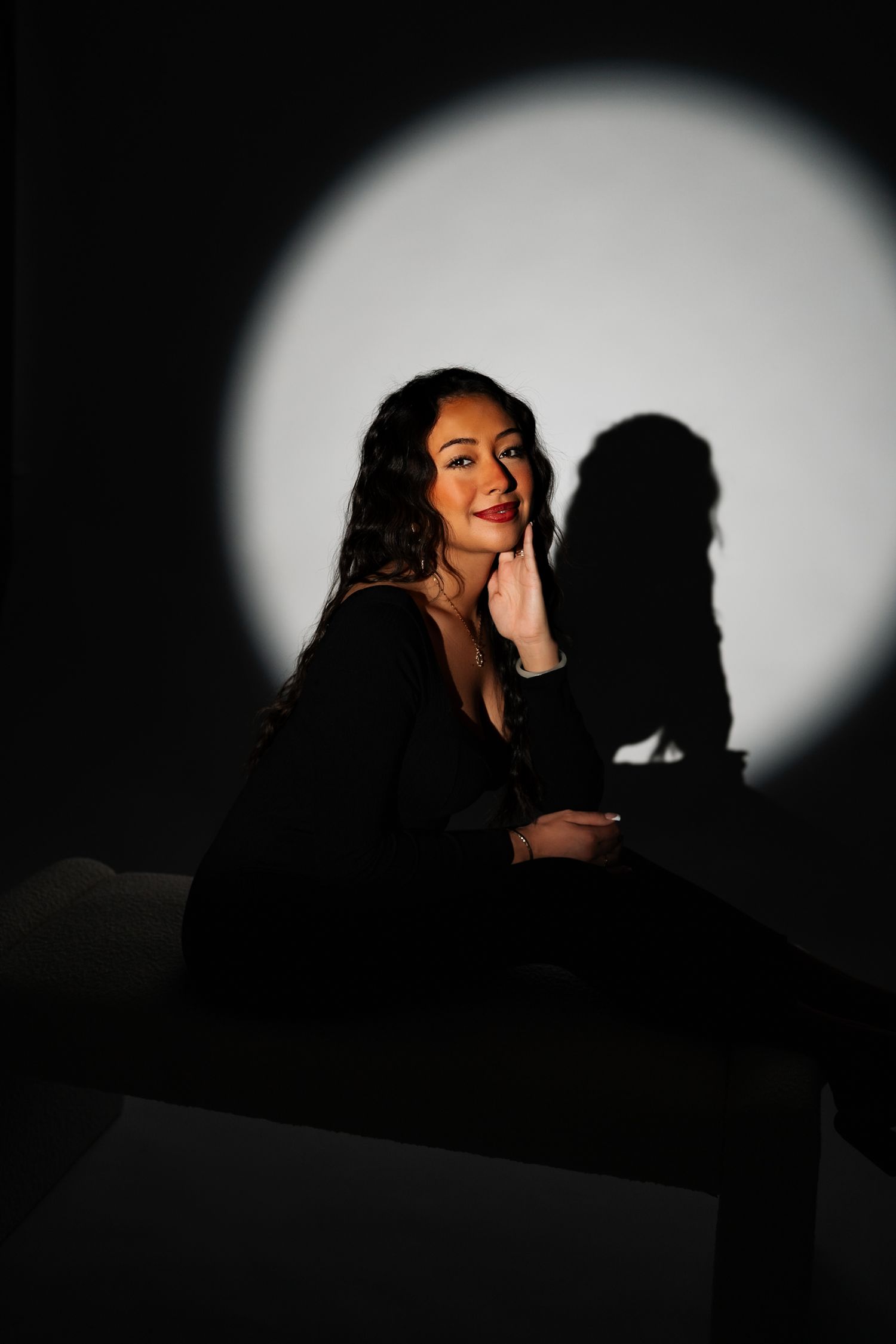 Artistic portrait with dramatic lighting showing a figure against a large white circular backdrop.