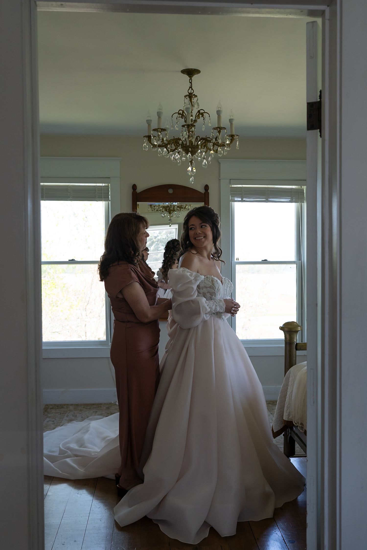 Wedding preparation scene showing a flowing white gown being fitted in a sunlit room.