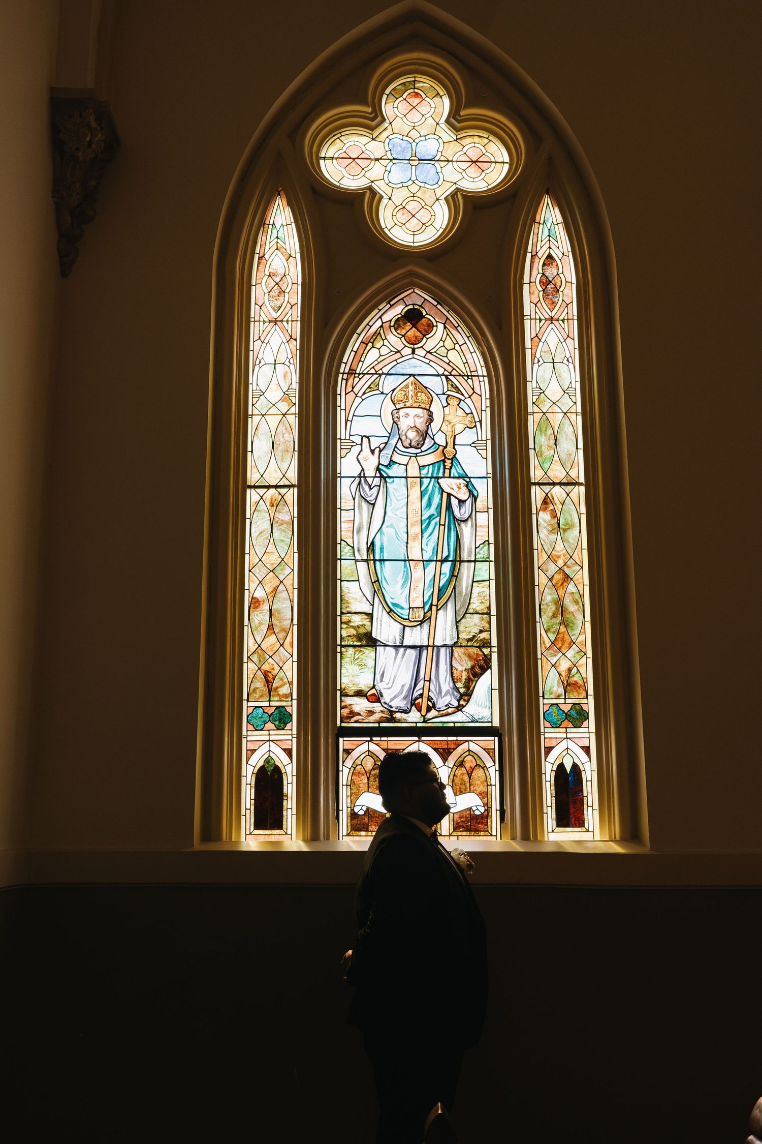 Silhouette against a beautiful stained glass church window depicting a religious figure.