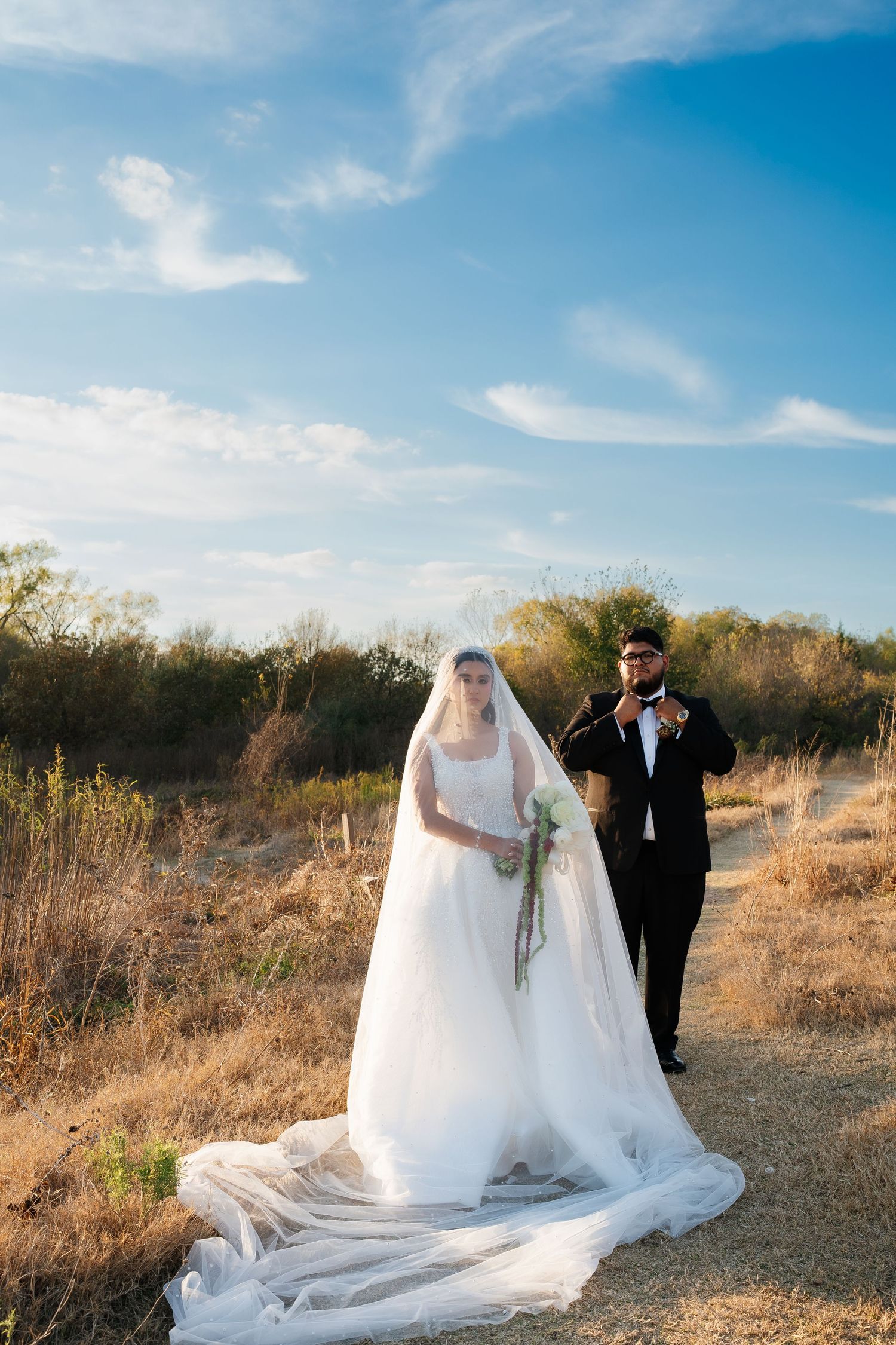 Newlyweds pose for photos in a scenic outdoor setting with blue skies and natural landscape.