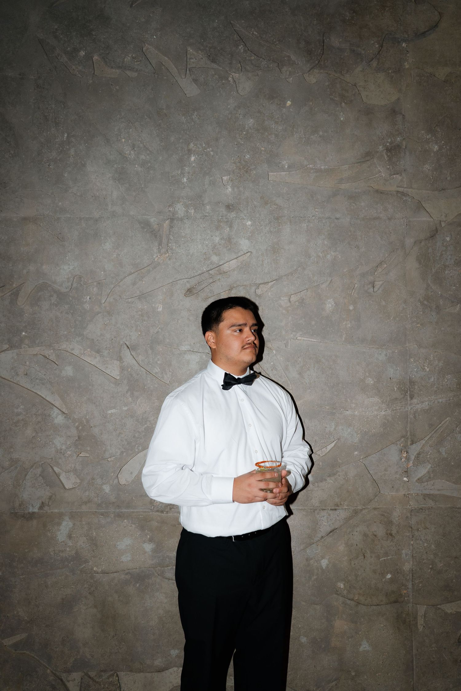 Person in formal black and white attire photographed against textured concrete wall.