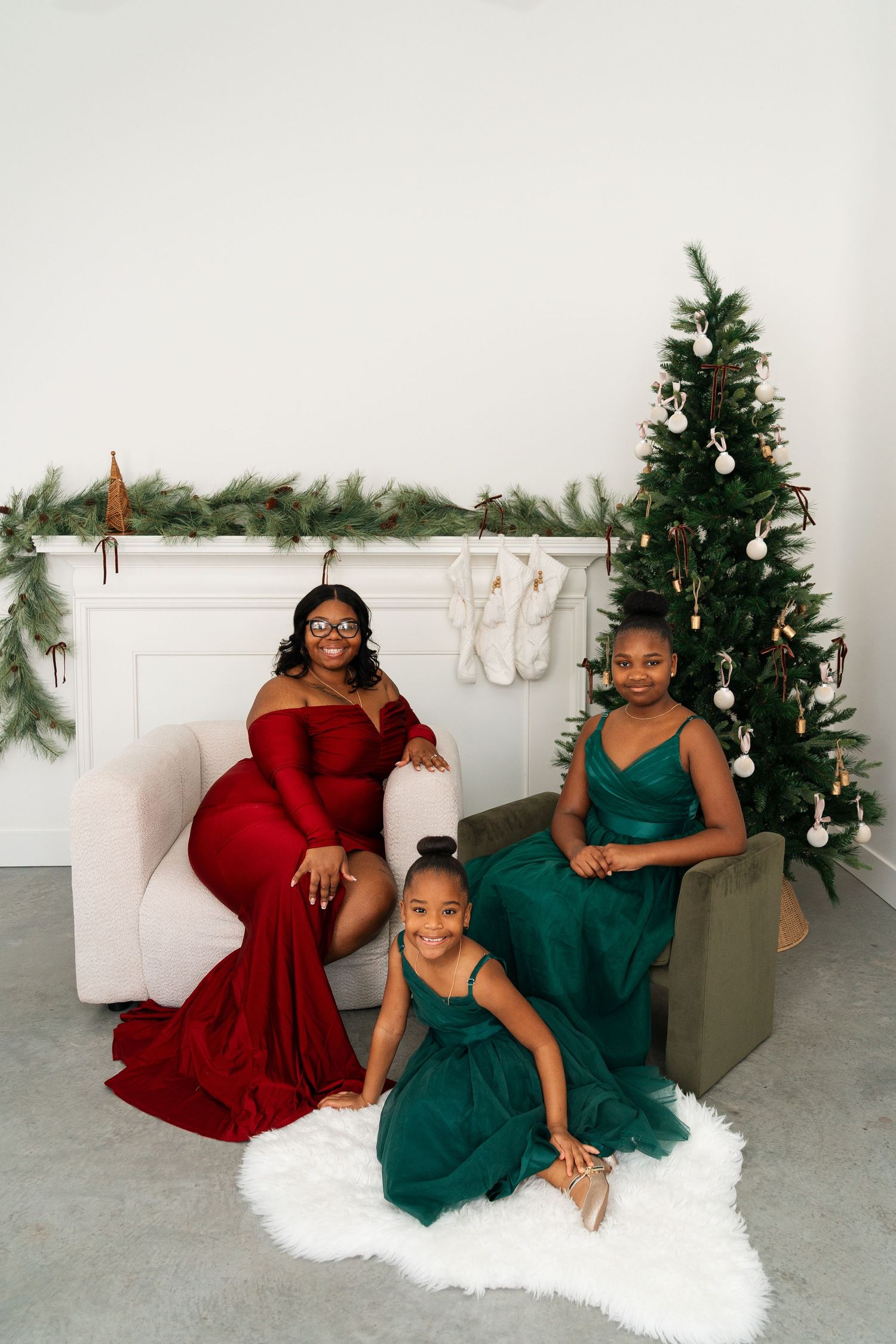 A group in red and green formal dresses poses in front of holiday decorations and a Christmas tree.