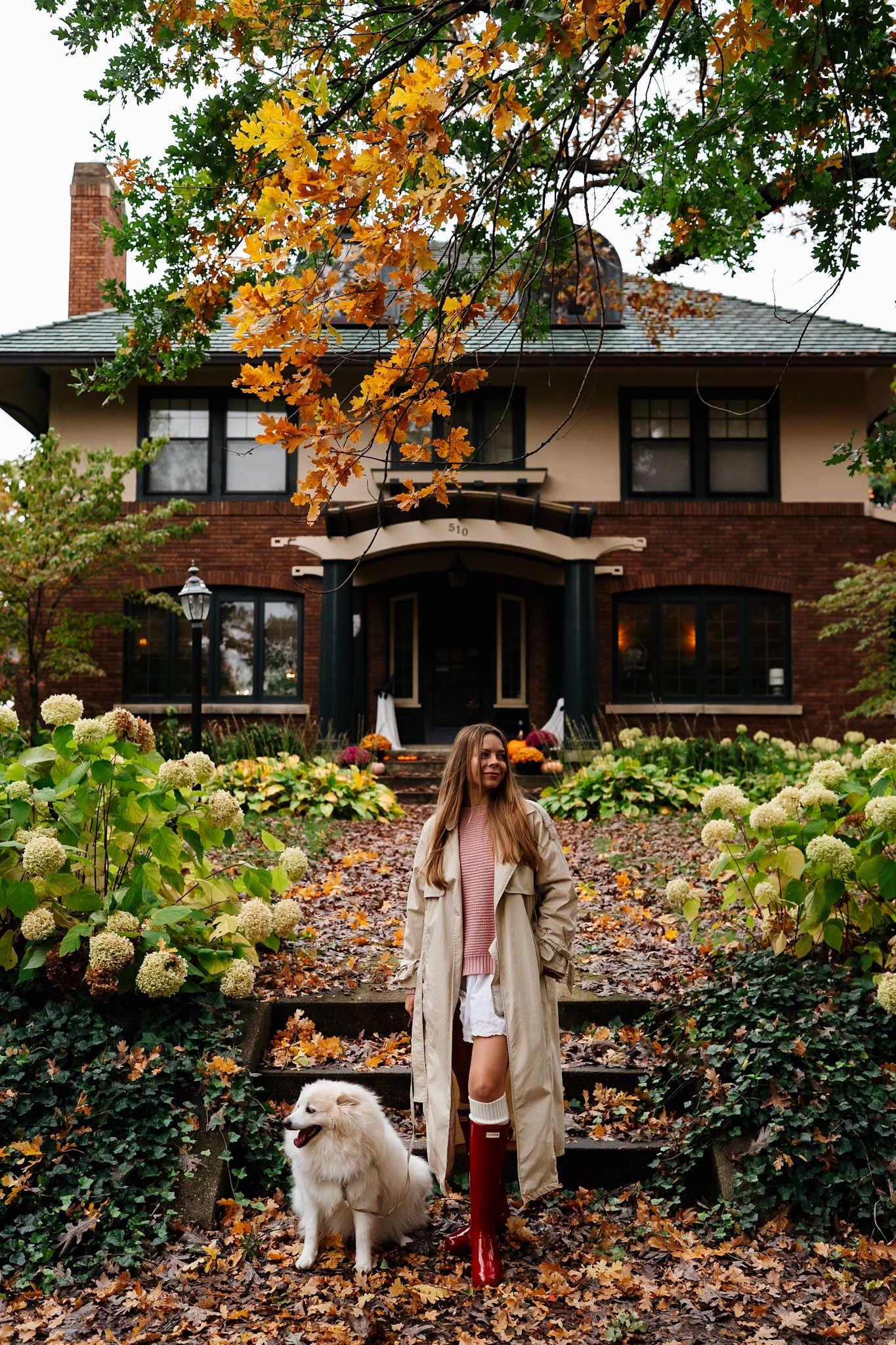 Lifestyle photography featuring a white fluffy dog and autumn fashion against a residential backdrop.