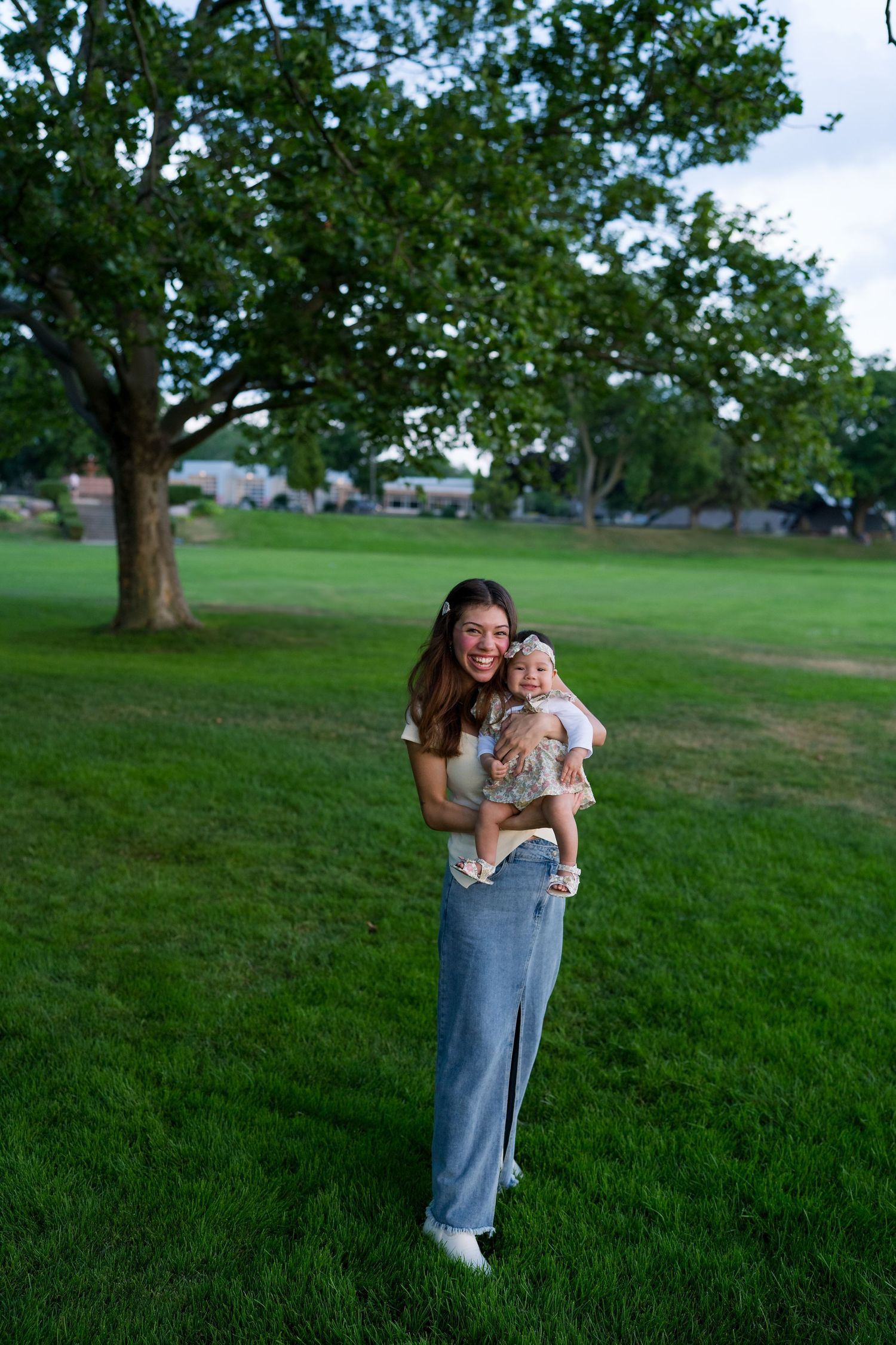 Mother and baby playing together on green grass field with trees in background.