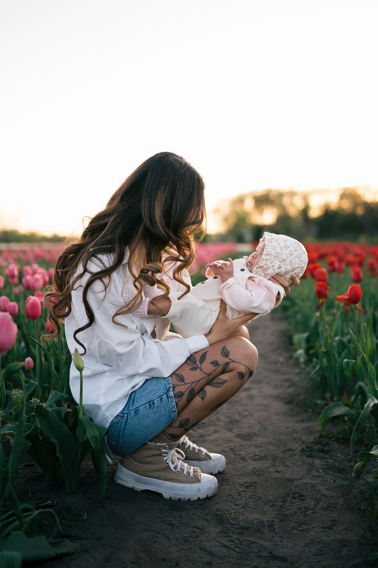 A person holding a baby among vibrant pink tulip fields at sunset.