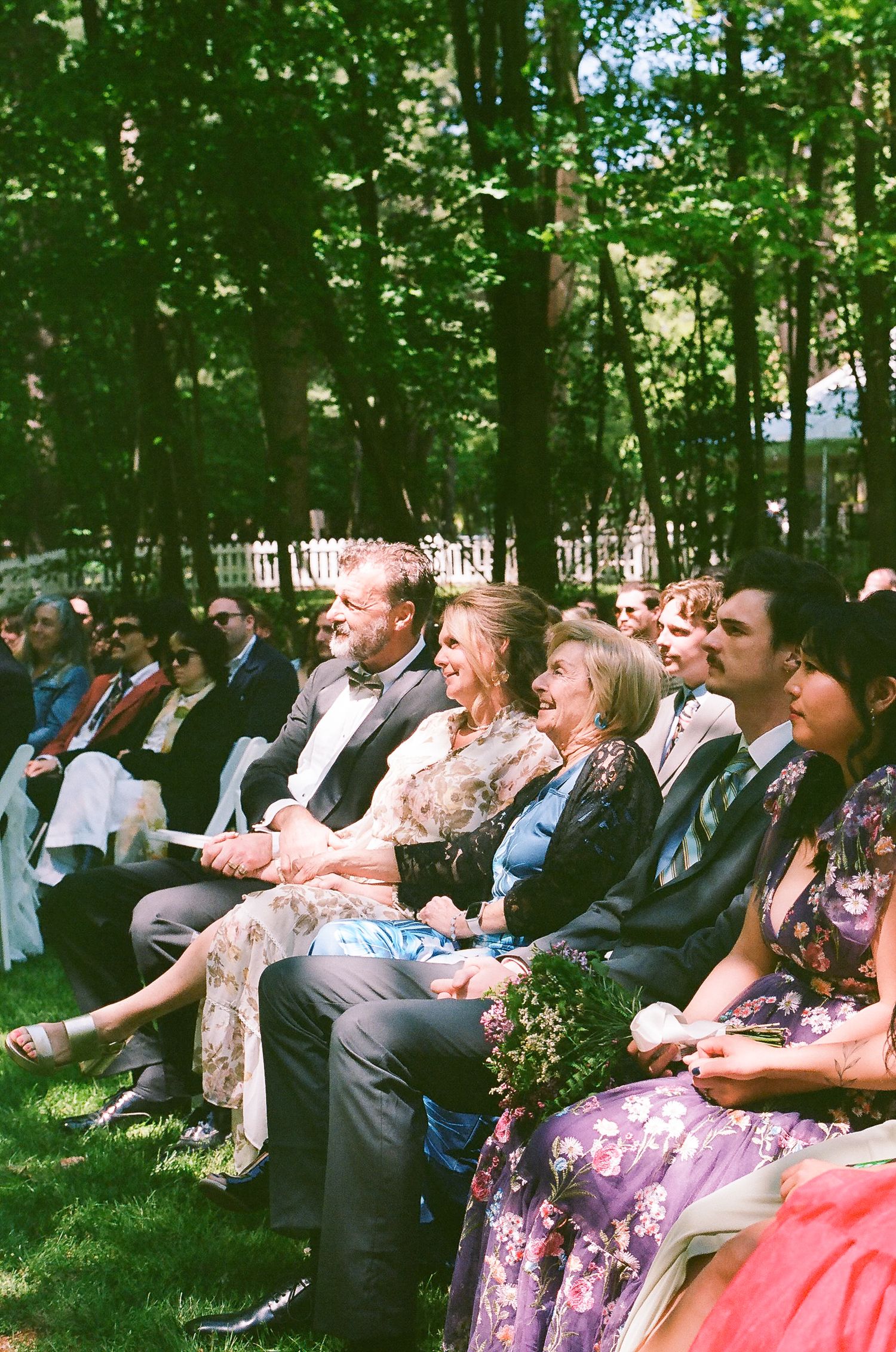 Wedding guests seated outdoors watching ceremony in wooded setting.