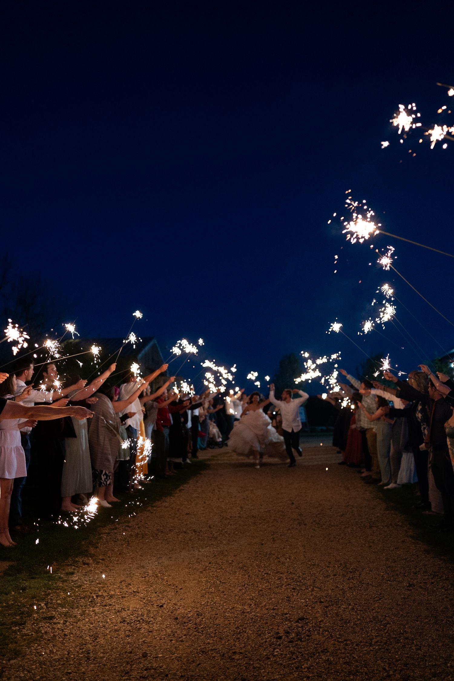 Wedding guests create a magical sparkler exit tunnel against the dark night sky.