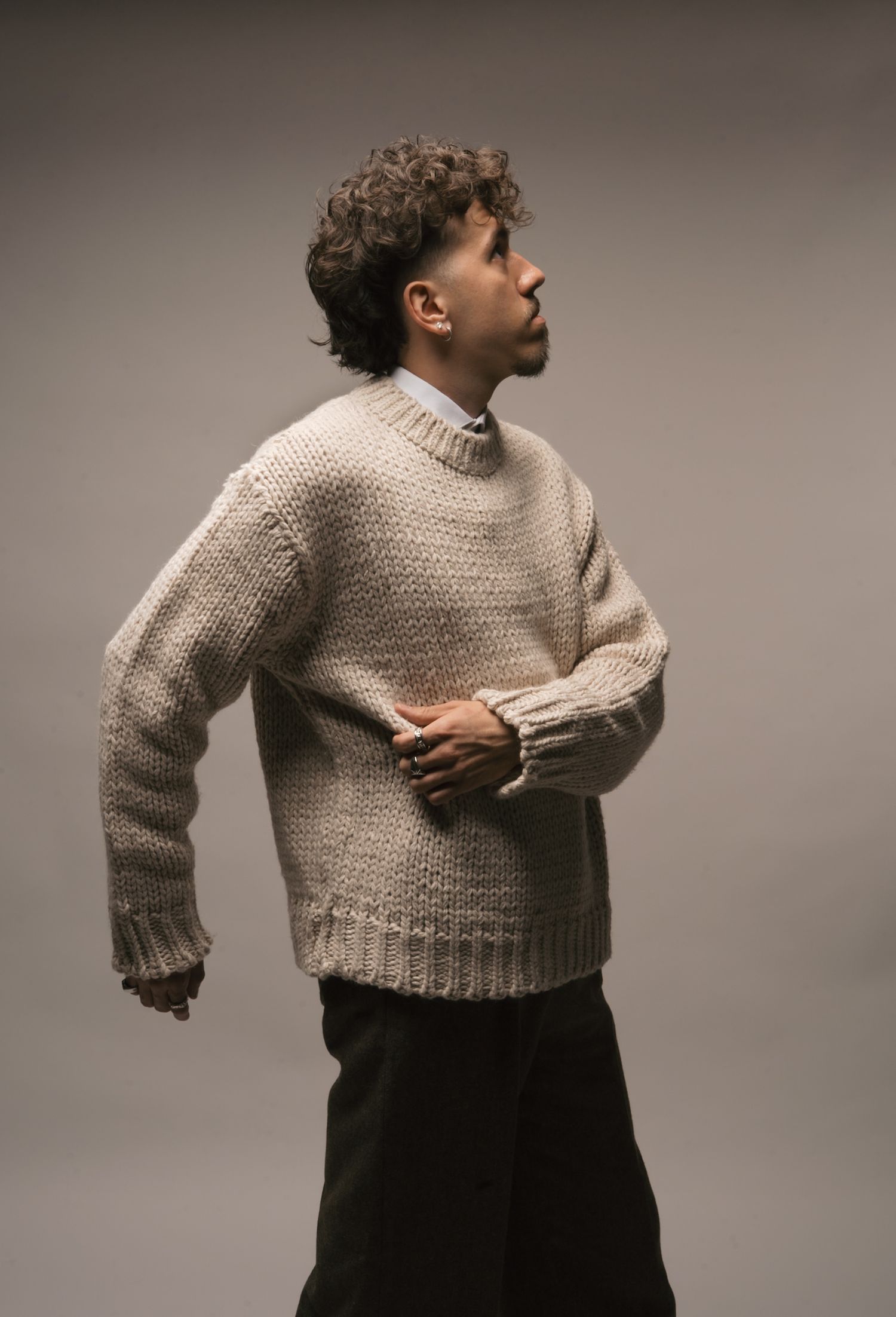 Fashion model poses in chunky beige knit sweater against neutral backdrop in artistic portrait series.