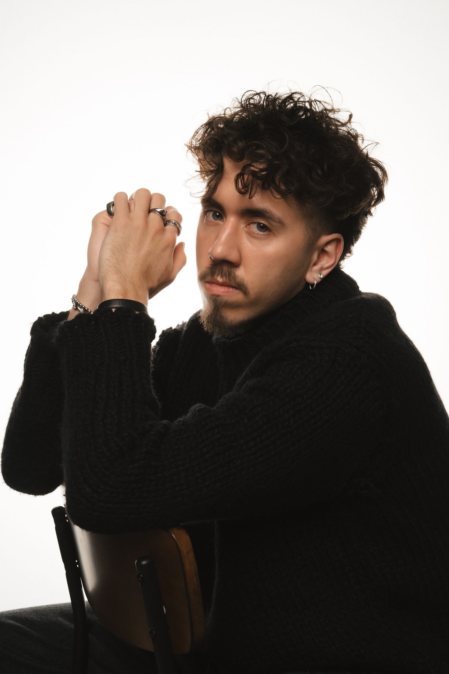 Fashion model poses dramatically in black knitwear against bright white studio backdrop.