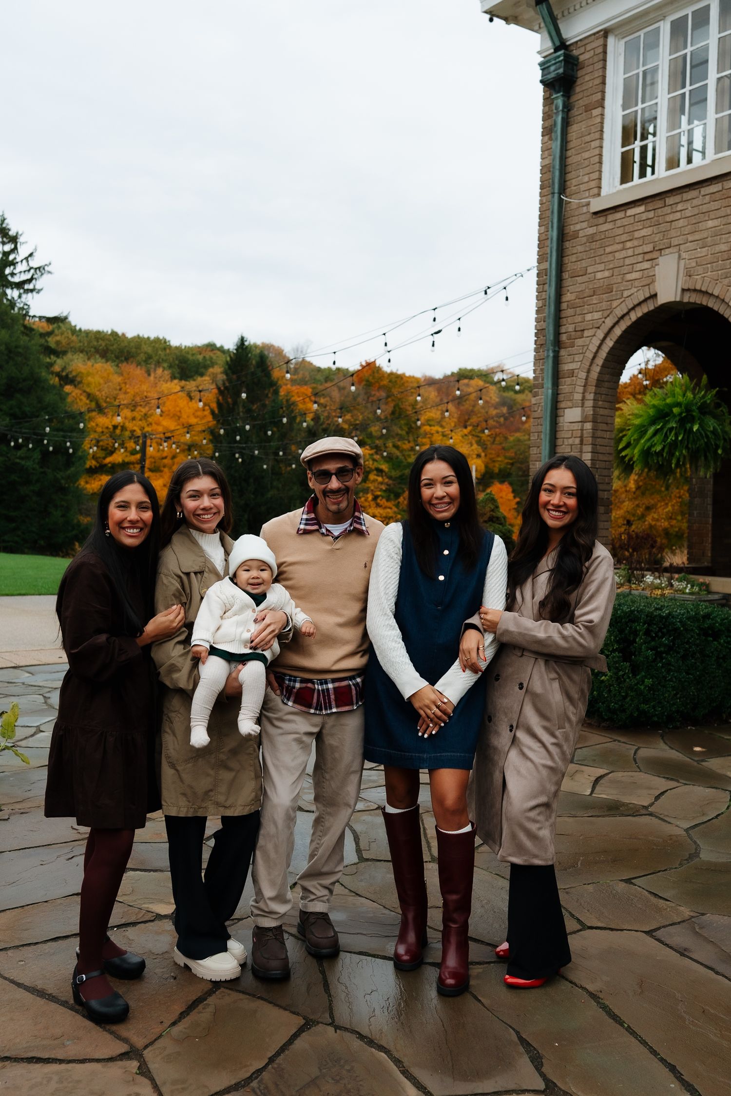 Family photo outdoors with brick building and autumn foliage in background.