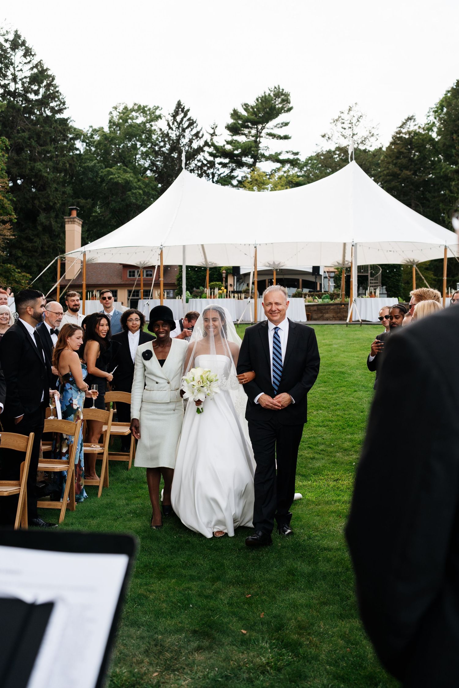 Outdoor wedding ceremony setup with white tents and wooden chairs on a manicured lawn.