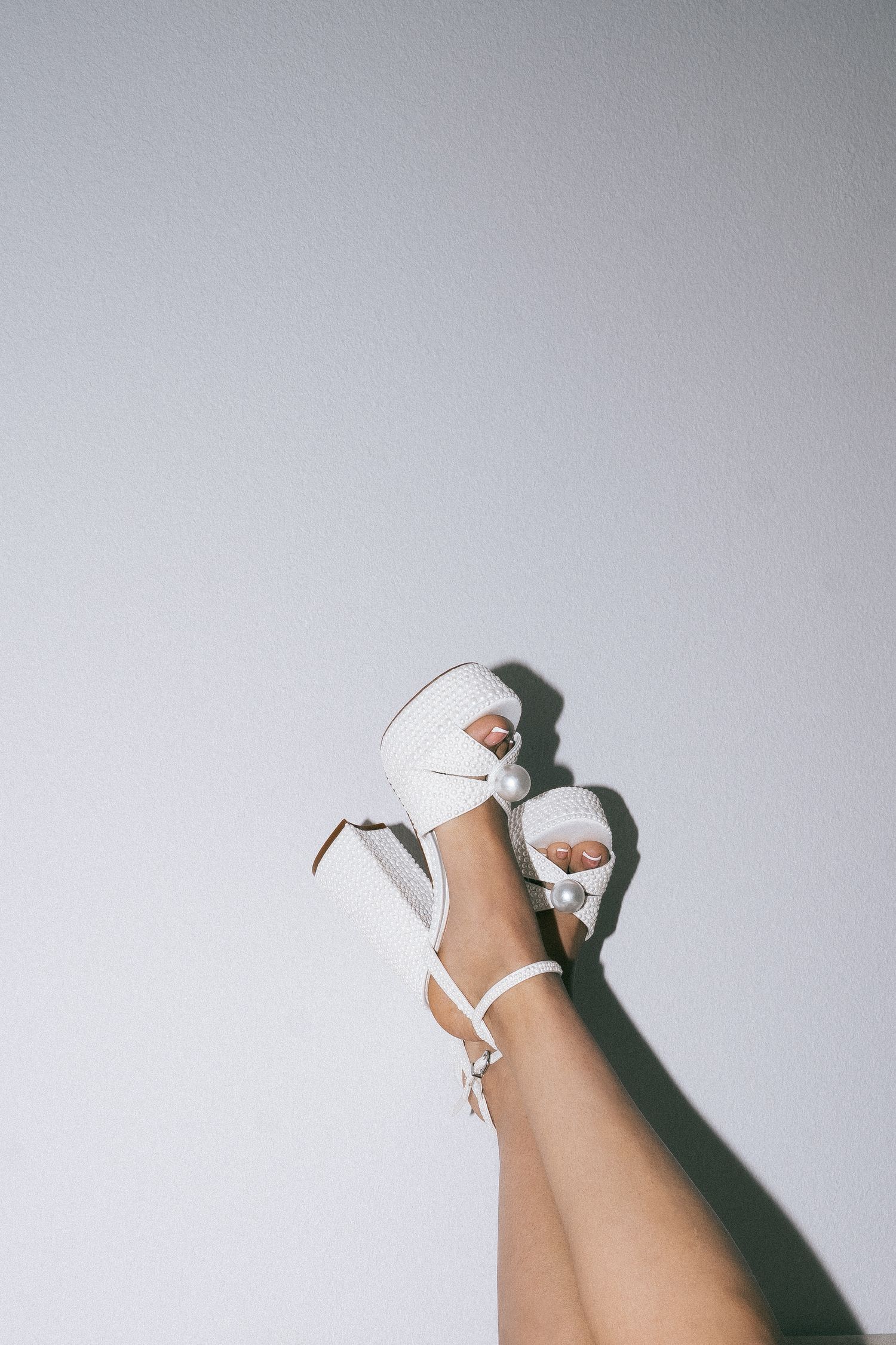 White high heel shoe photographed against a light gray background.