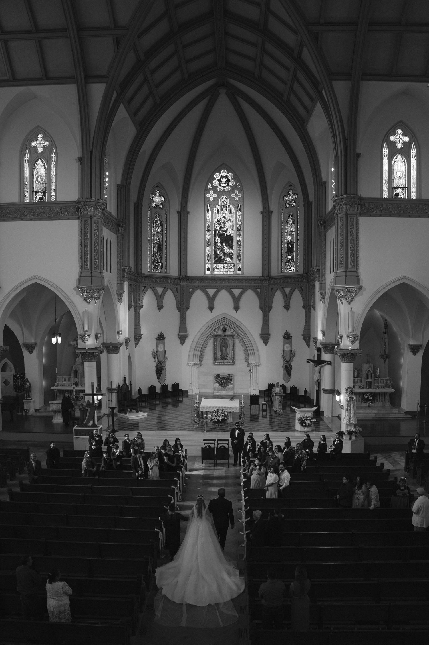 Black and white panorama of a church wedding ceremony with guests seated in wooden pews.