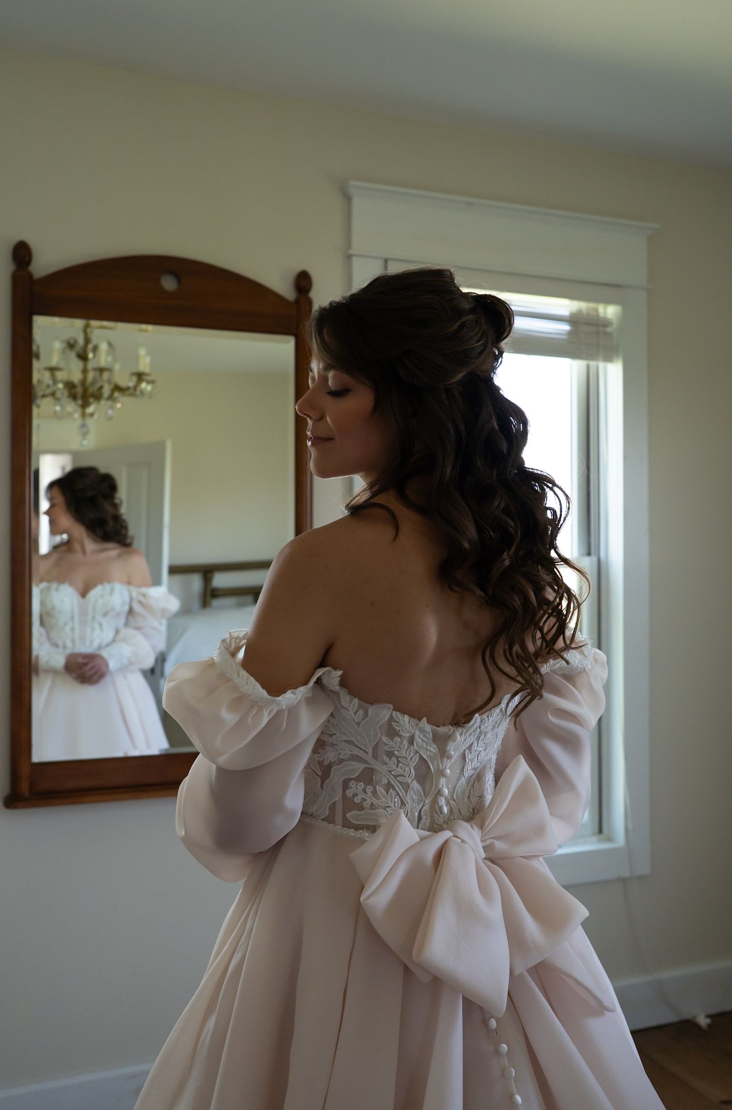 Close-up detail of a white wedding dress with lace and bow accents in soft natural light.