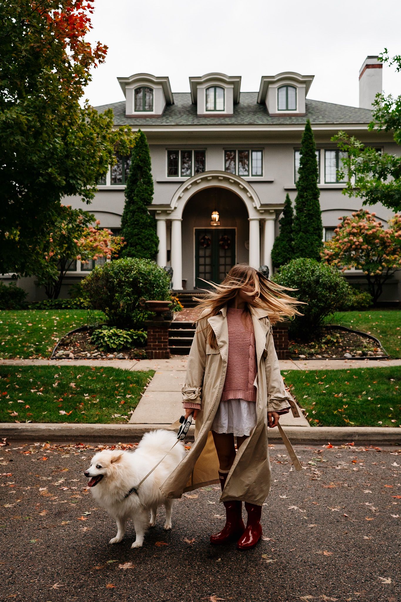 Elegant fall fashion shoot with a white dog in front of a grand white mansion with arched doorways.