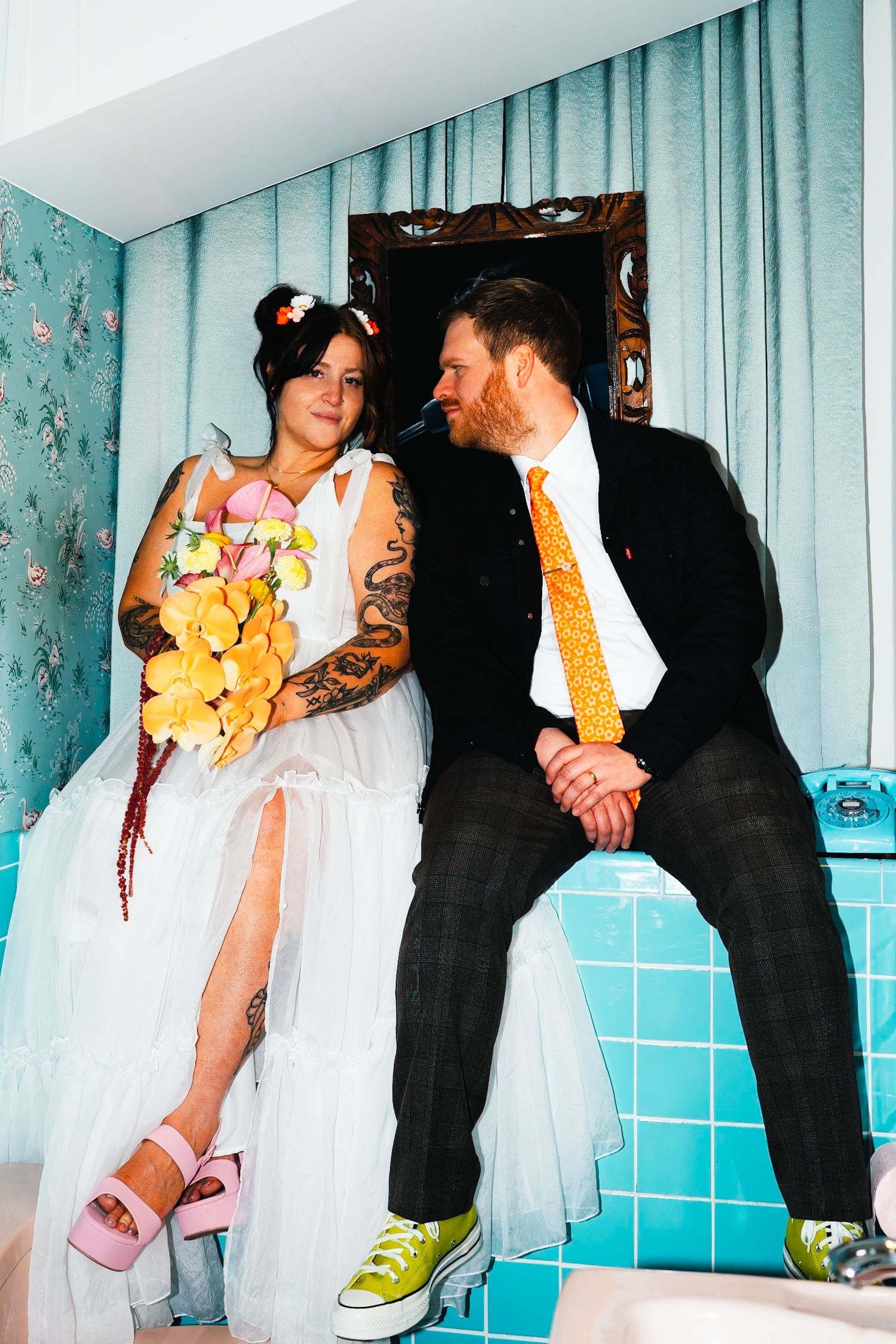 A couple in wedding attire sitting casually with contrasting pink sandals and yellow sneakers.