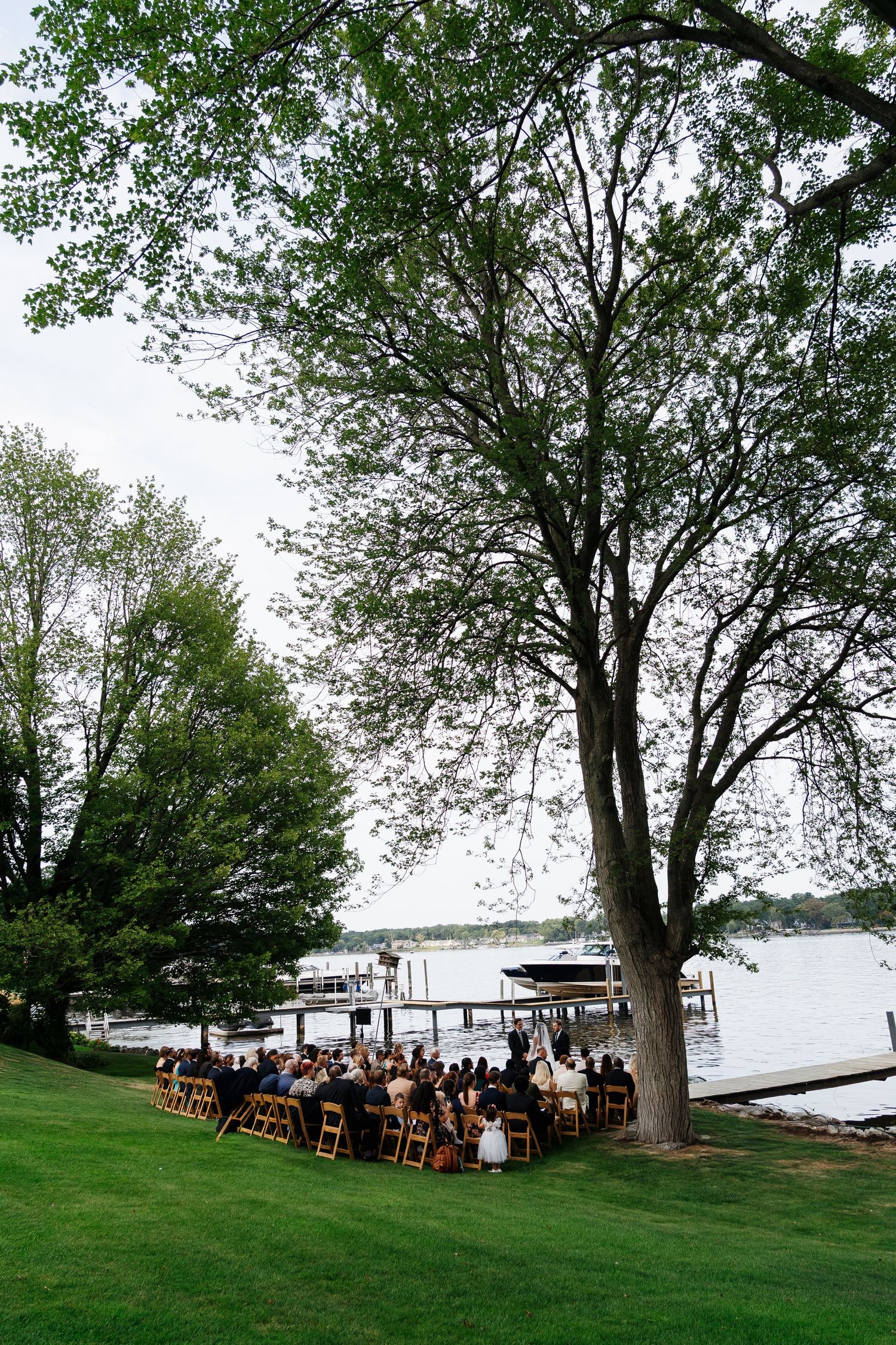 Rows of wooden chairs set up on a grassy lawn near a waterfront for an outdoor wedding ceremony.