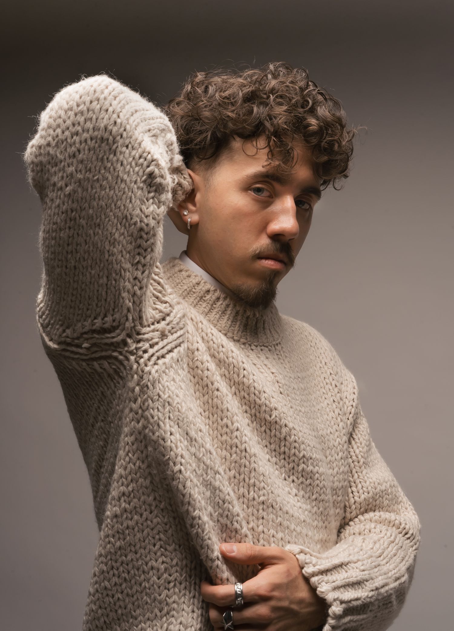 Person wearing oversized cream turtleneck sweater poses expressively in studio lighting.