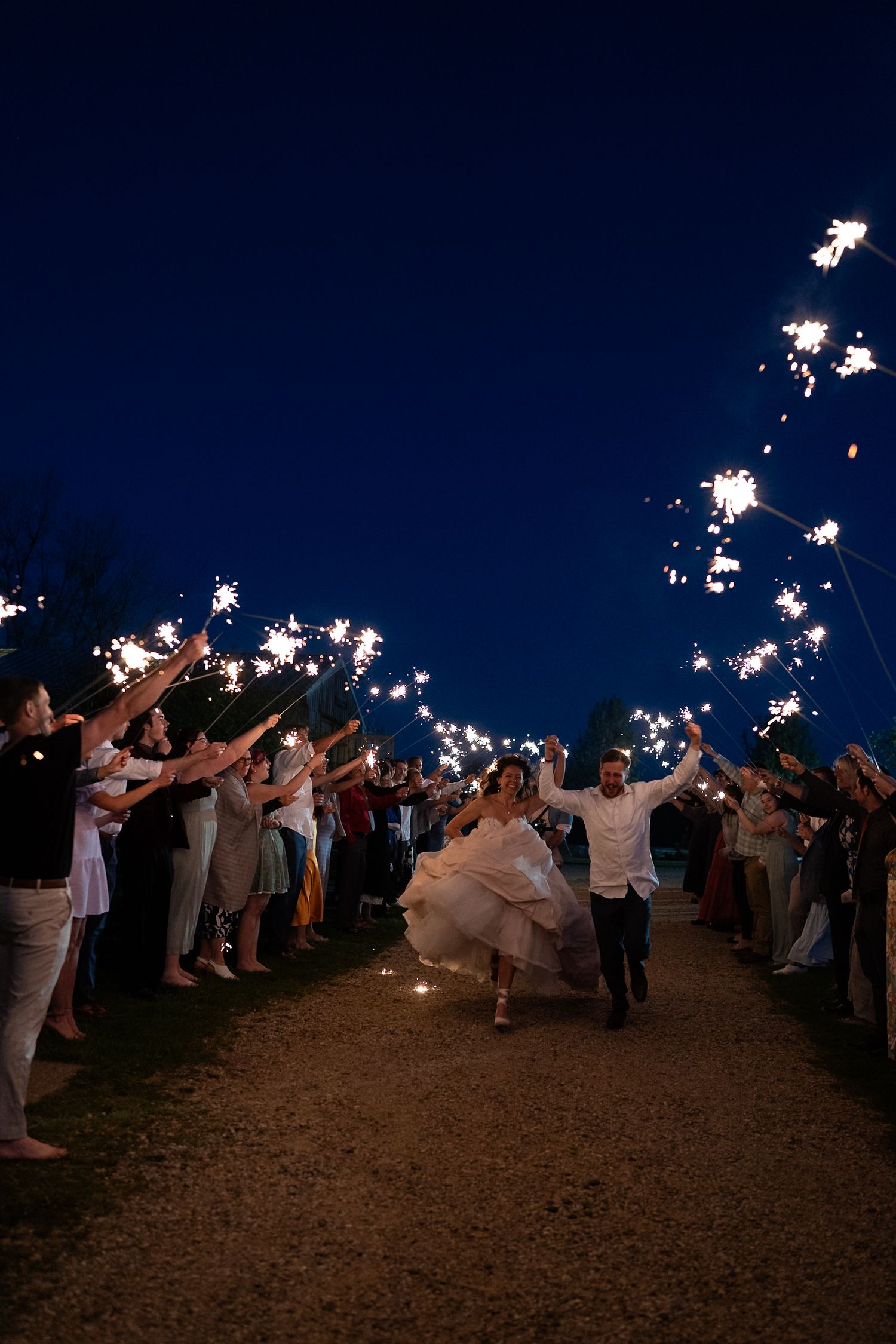 Wedding guests hold sparklers in a nighttime celebration creating a magical tunnel of light.