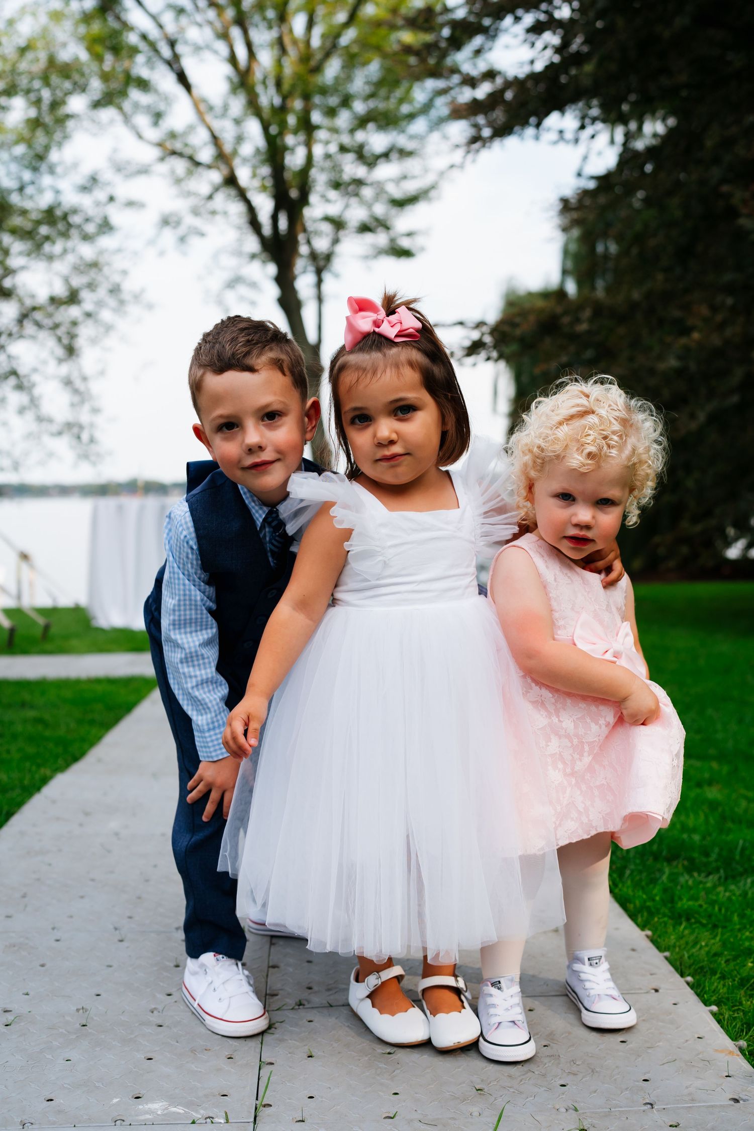 Young children in formal wedding attire sitting together on outdoor steps.