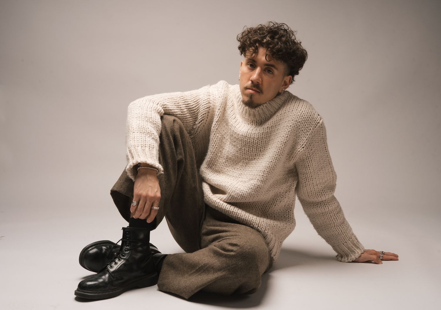 Figure in cream sweater poses on floor in minimalist studio setting.