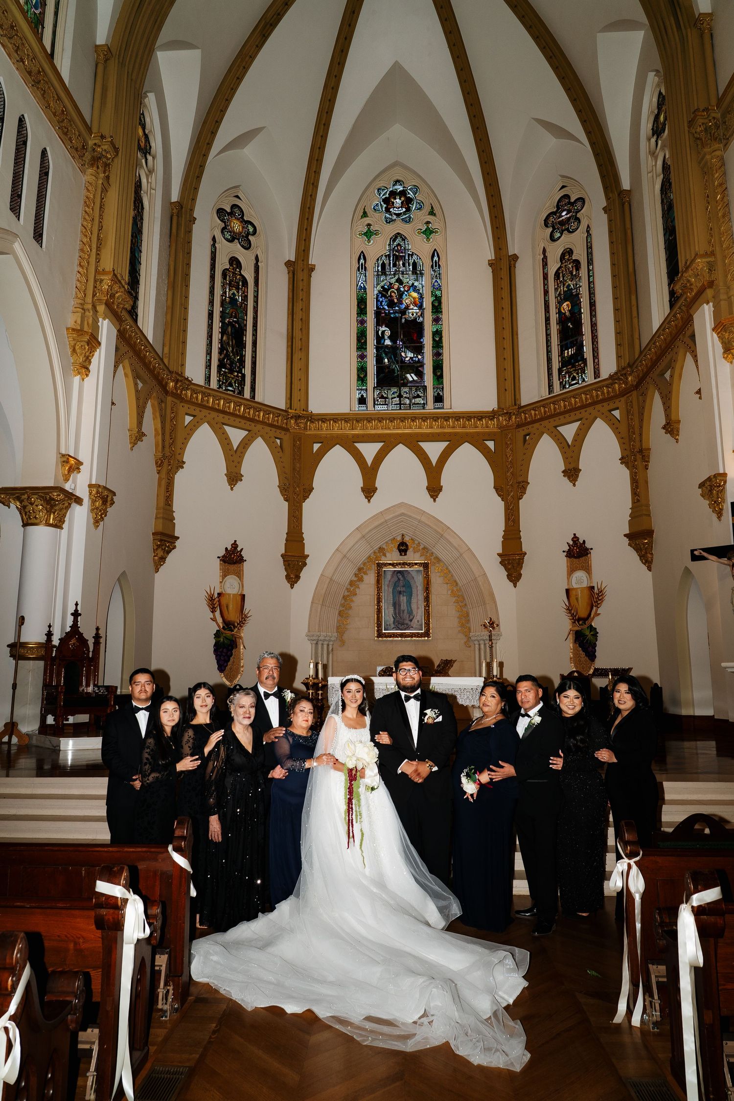 A wedding party posed in formal attire inside a grand cathedral with gothic architecture.