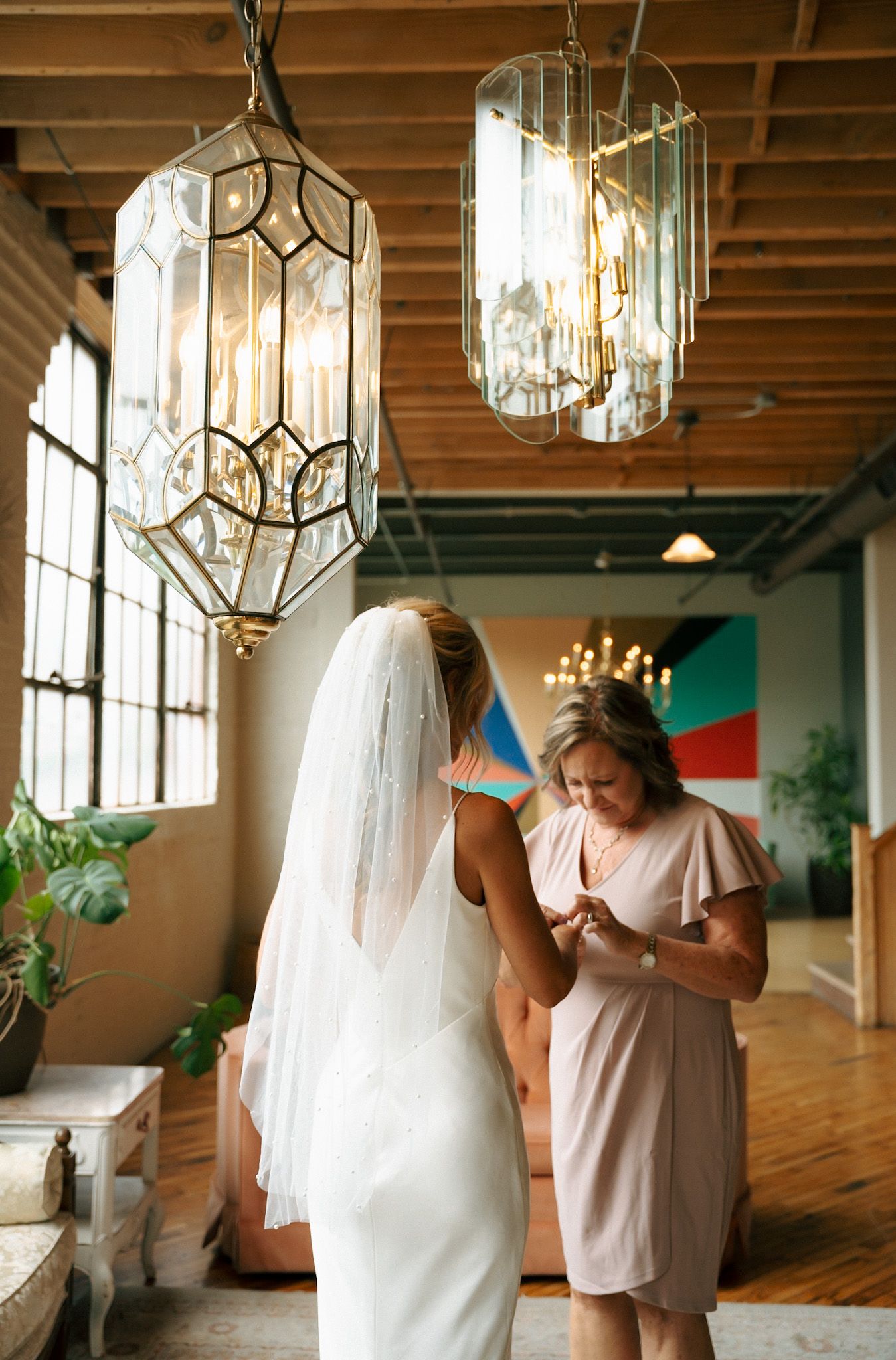 Wedding dress preparations under crystal chandeliers in a rustic-industrial venue.