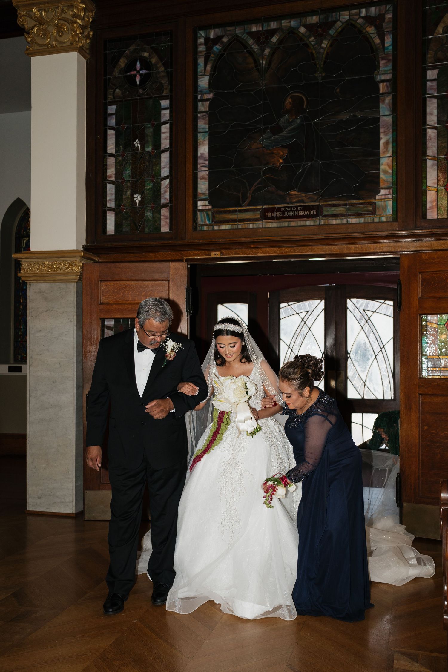 Wedding party gathers in an elegant church interior with stained glass windows and wooden details.