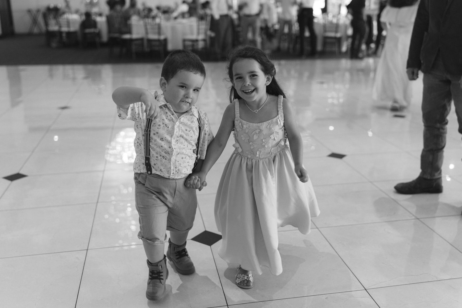 Children in formal attire running and playing together on a shiny white floor at an indoor event.