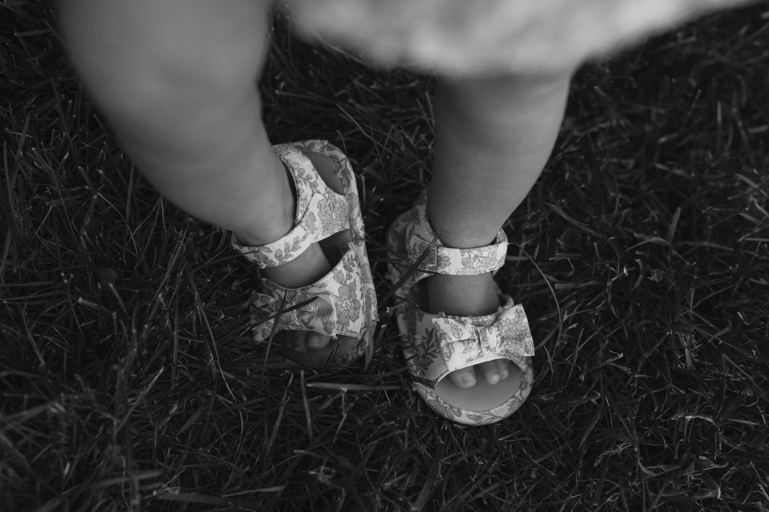 Close-up of baby shoes and feet on dark ground.