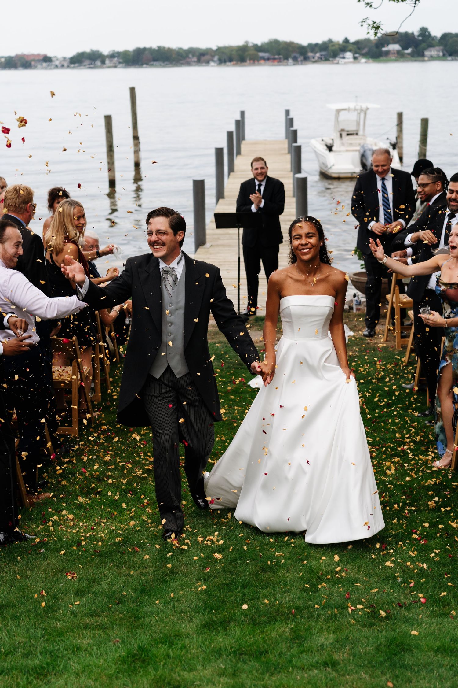 Wedding celebration on waterfront lawn with confetti being thrown as guests cheer.