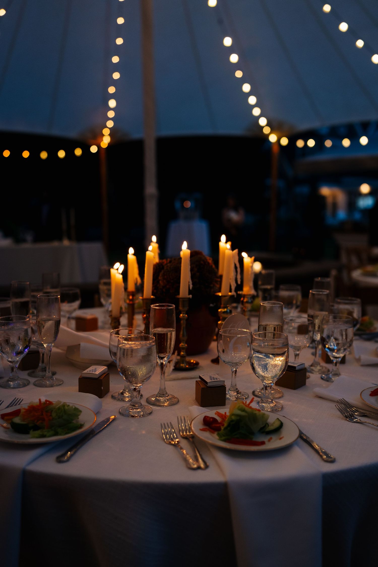 Romantic candlelit wedding reception table setting with glowing string lights above.