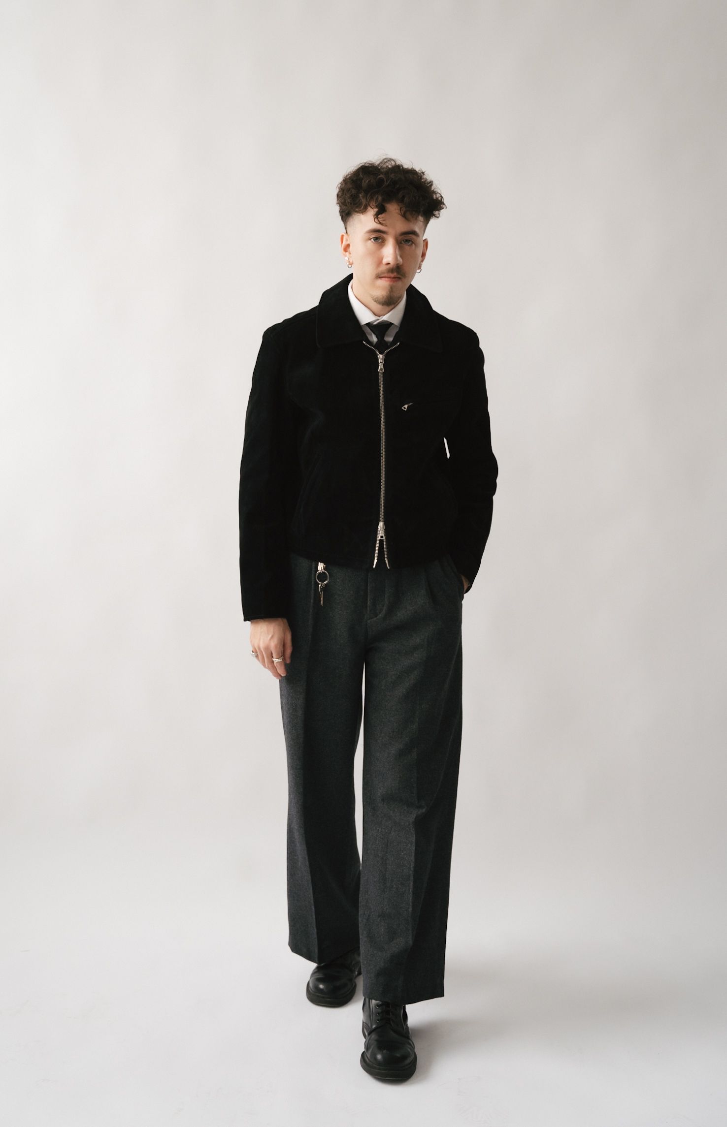 Model wearing all black outfit stands against white background in full-length fashion photograph.