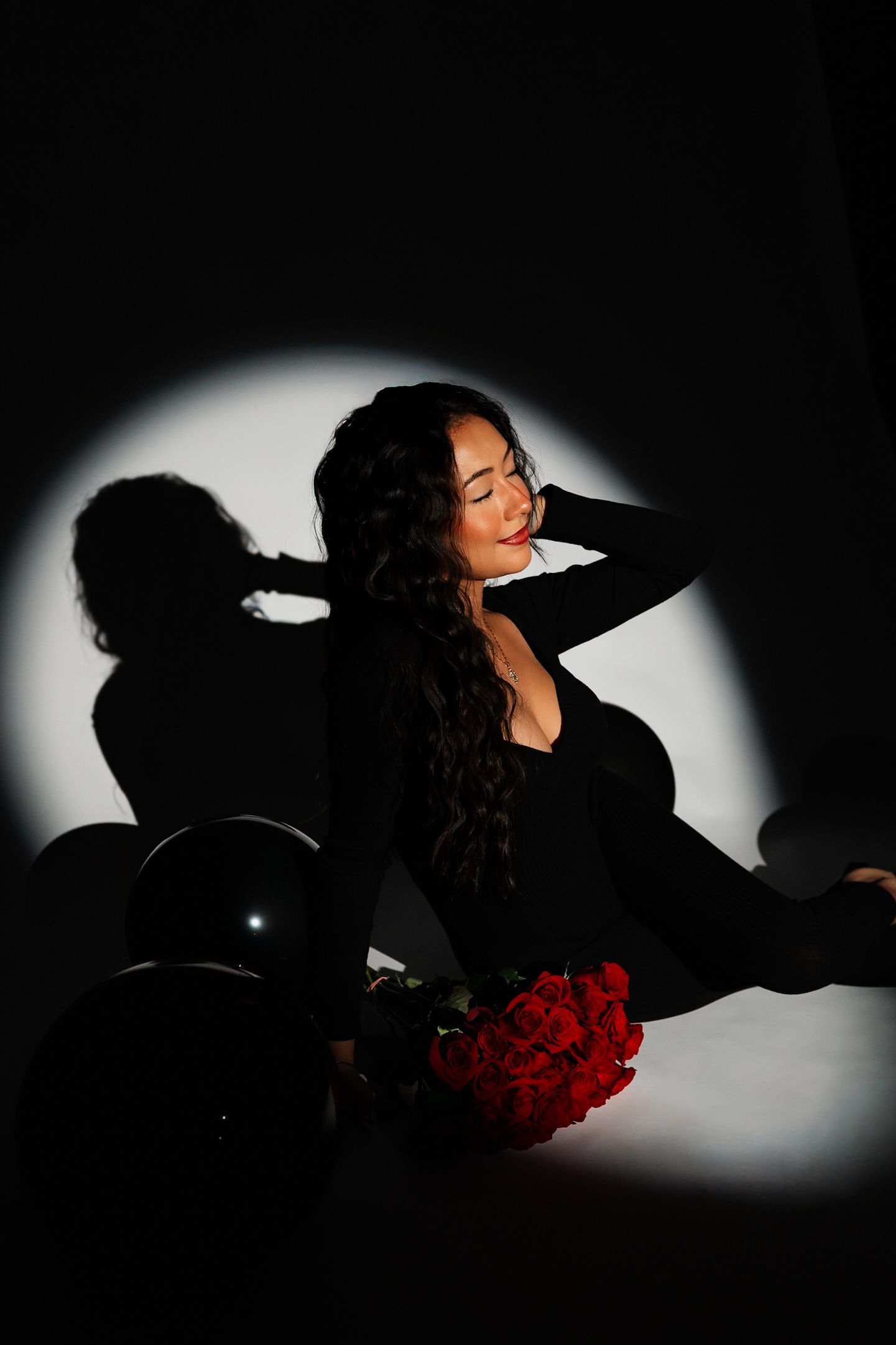 Artistic portrait with red roses and dramatic shadows in studio setting.