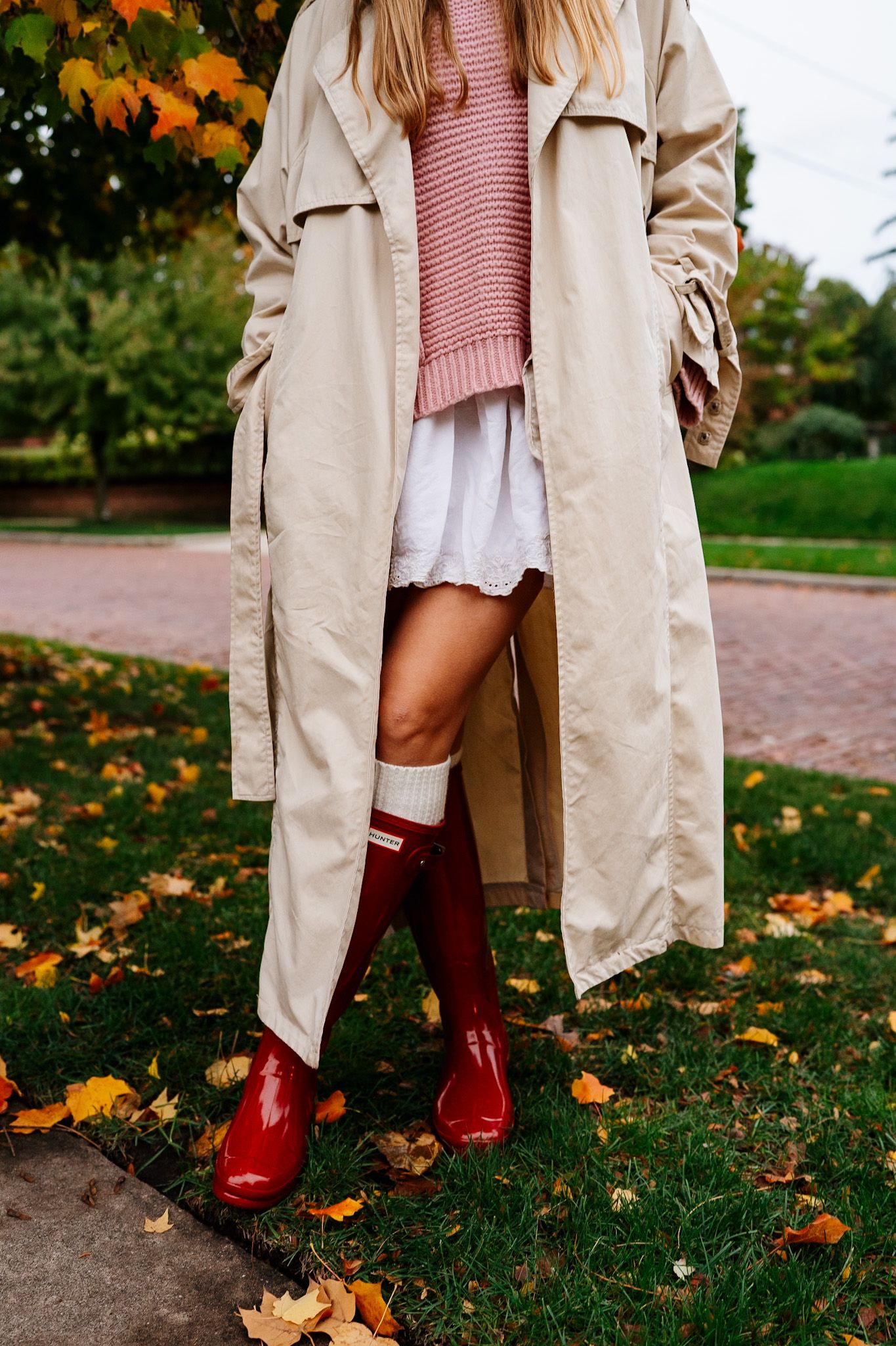 Stylish outfit detail showing beige coat and red boots against autumn ground.