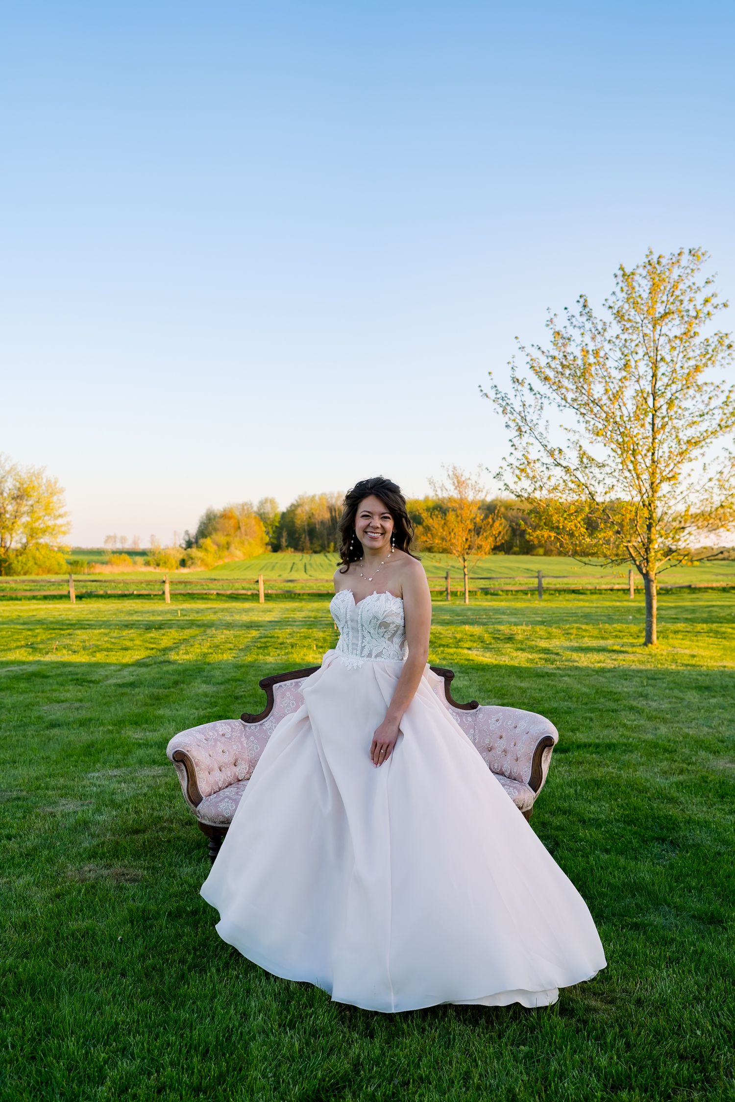 A stunning bridal portrait session in a sunlit field with a vintage sofa.