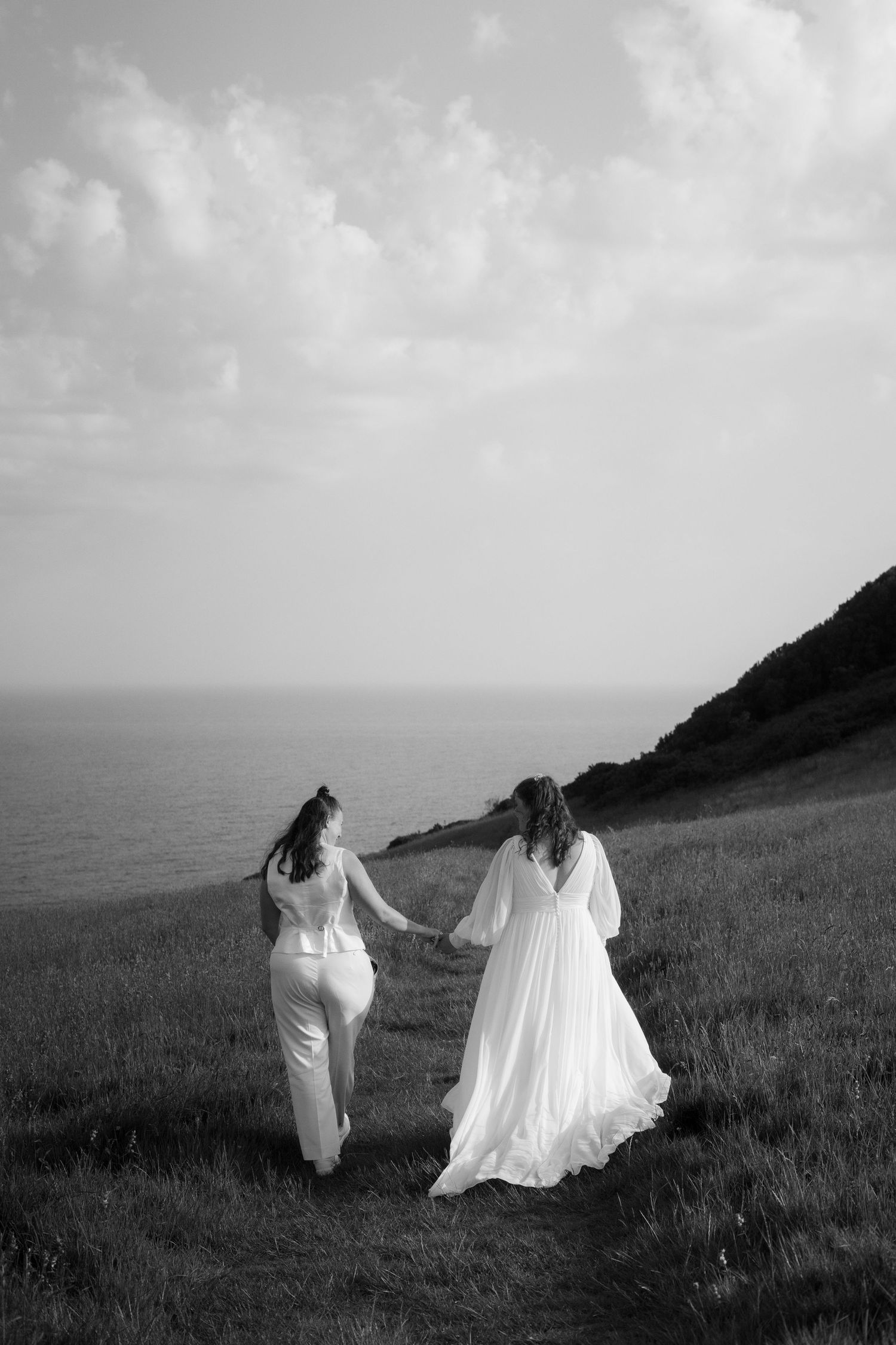 Bride and bride walking holding hands along the Cornish coast after Tredudwell Manor wedding