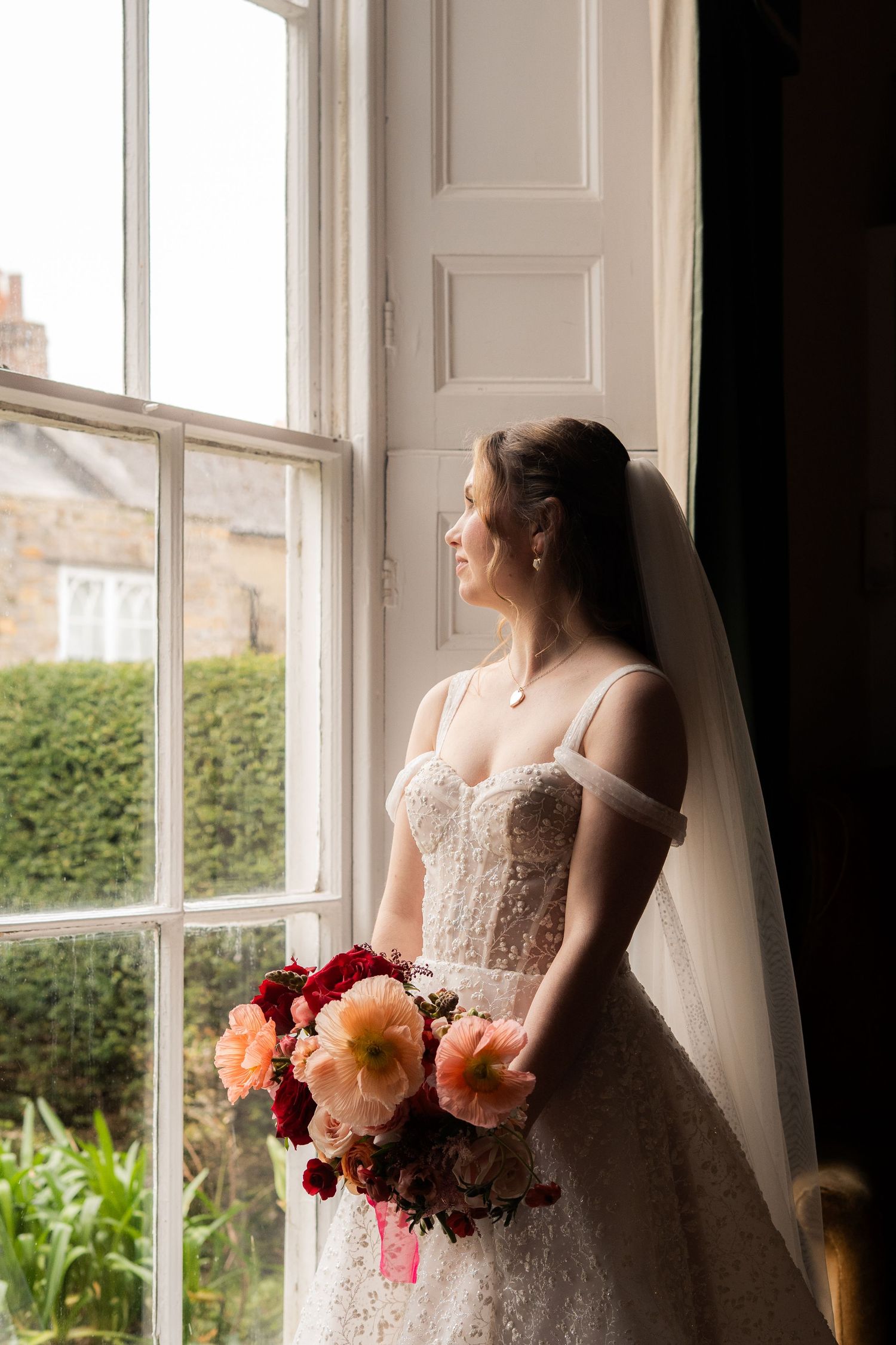 Editorial portrait of bride looking out of the window whilst getting ready in Penzance, Cornwall