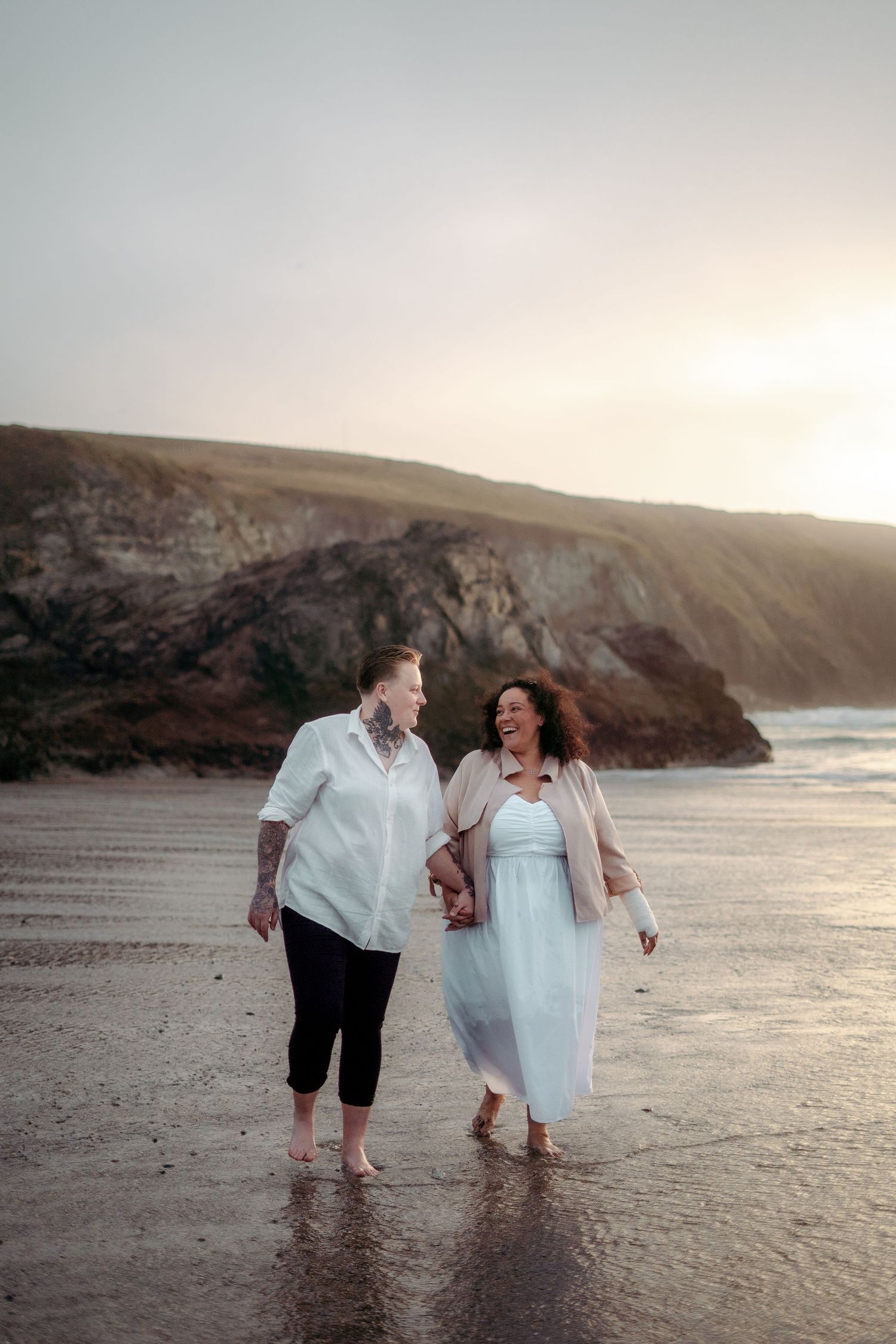 A lesbian couple walking hand in hand on the beach in Cornwall after getting engaged on Holywell Bay Beach