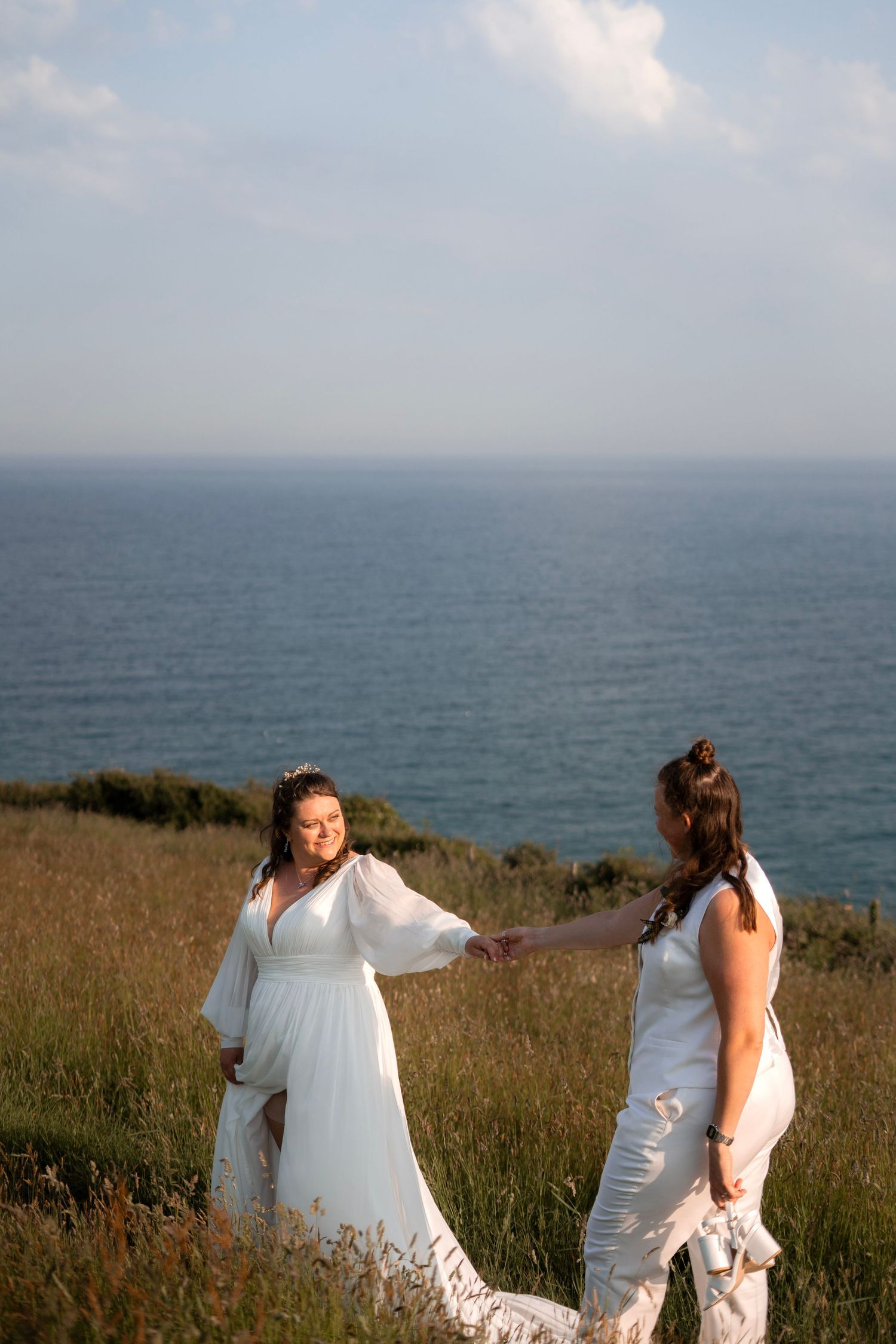 Bride and bride holding hands along the dramatic coastline of Lantivet Bay near Tredudwell Manor